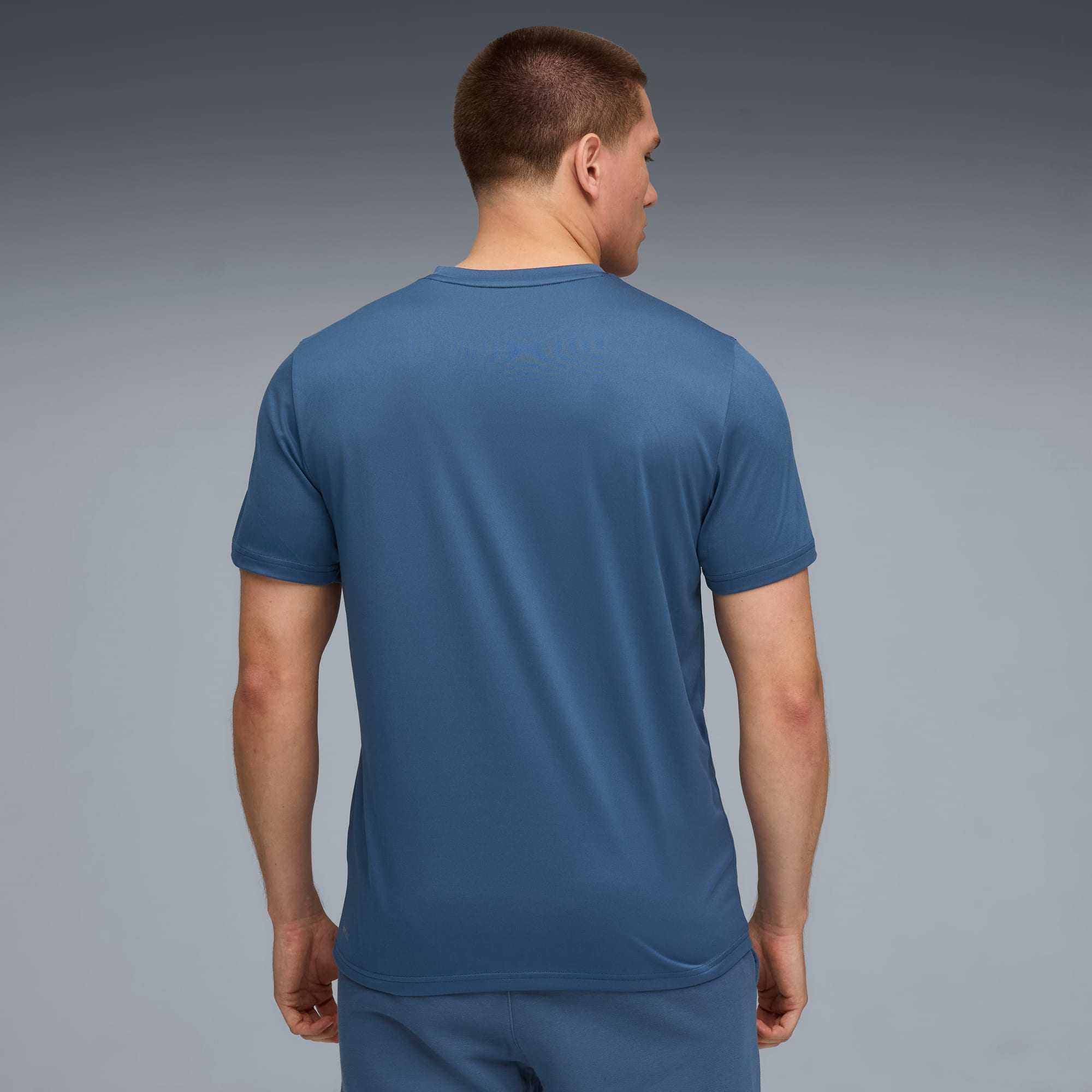 Un modèle, de dos sur fond gris, porte un t-shirt bleu.