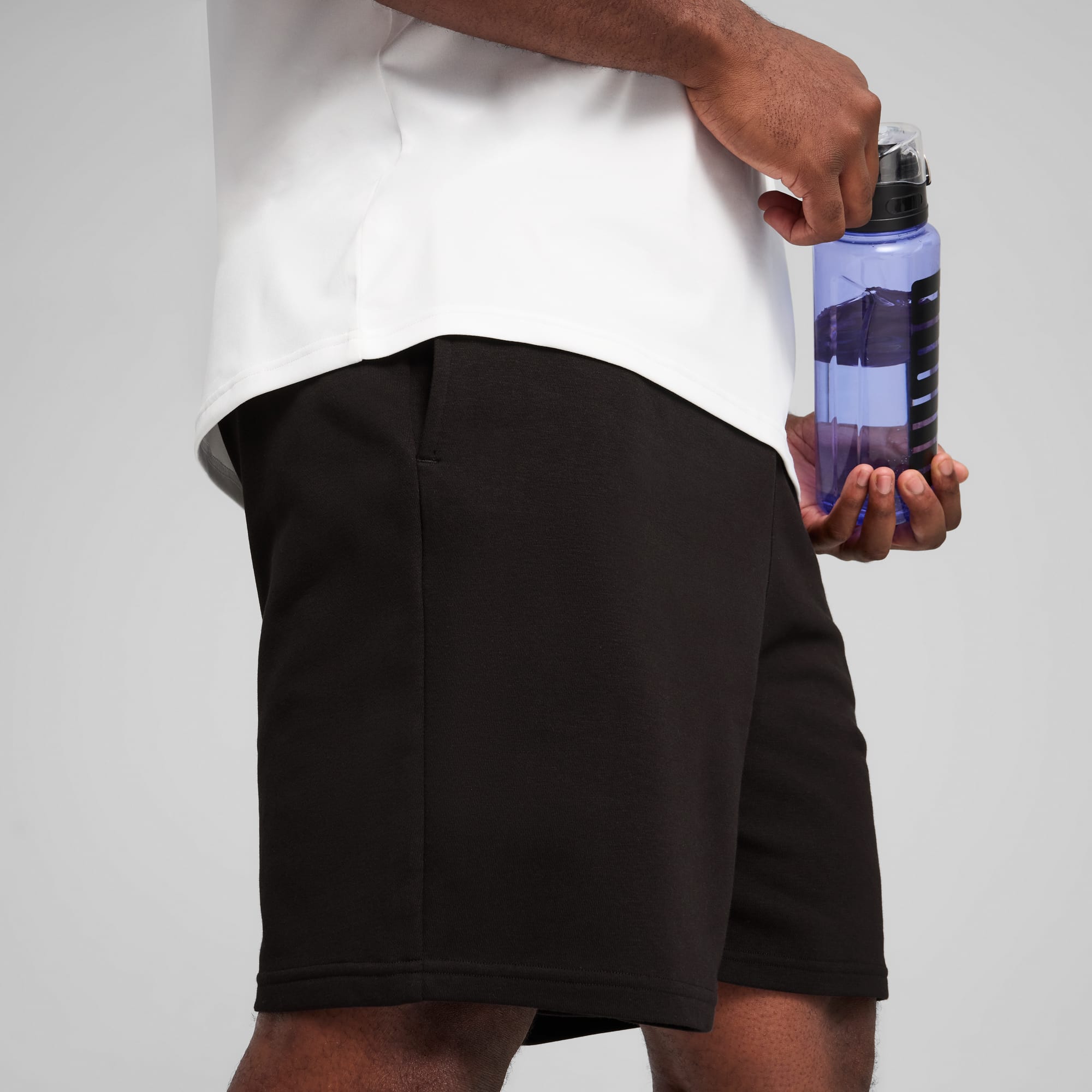 Su sfondo grigio, un modello tiene una borraccia blu, indossando top bianco e pantaloncini scuri.