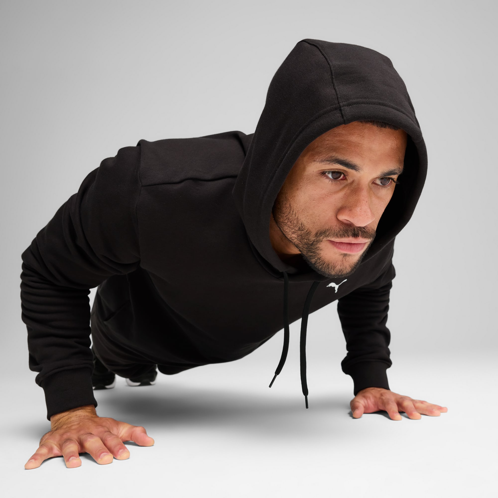 Een model in een zwarte hoodie doet push-ups tegen een grijze achtergrond.