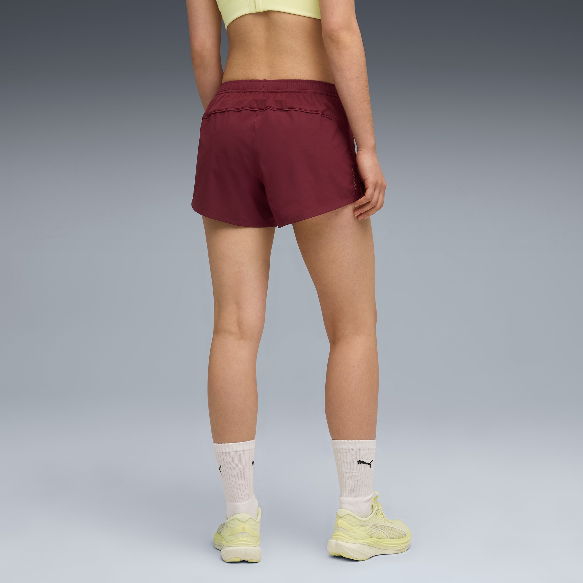 Sur fond gris, un mannequin porte short rouge, haut et chaussures jaunes, et chaussettes blanches.