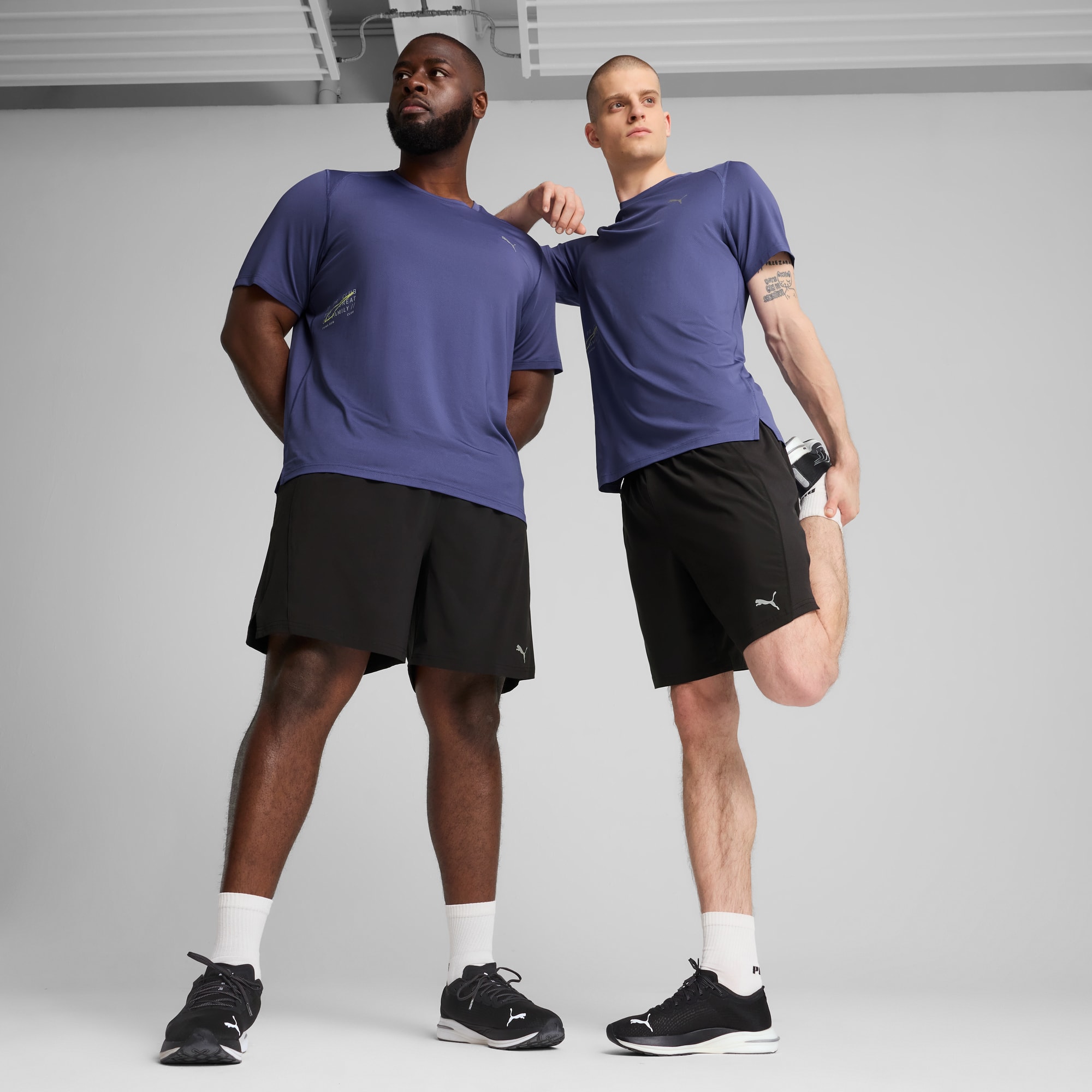 Twee modellen poseren tegen een grijze achtergrond, gekleed in blauwe t-shirts en zwarte shorts.