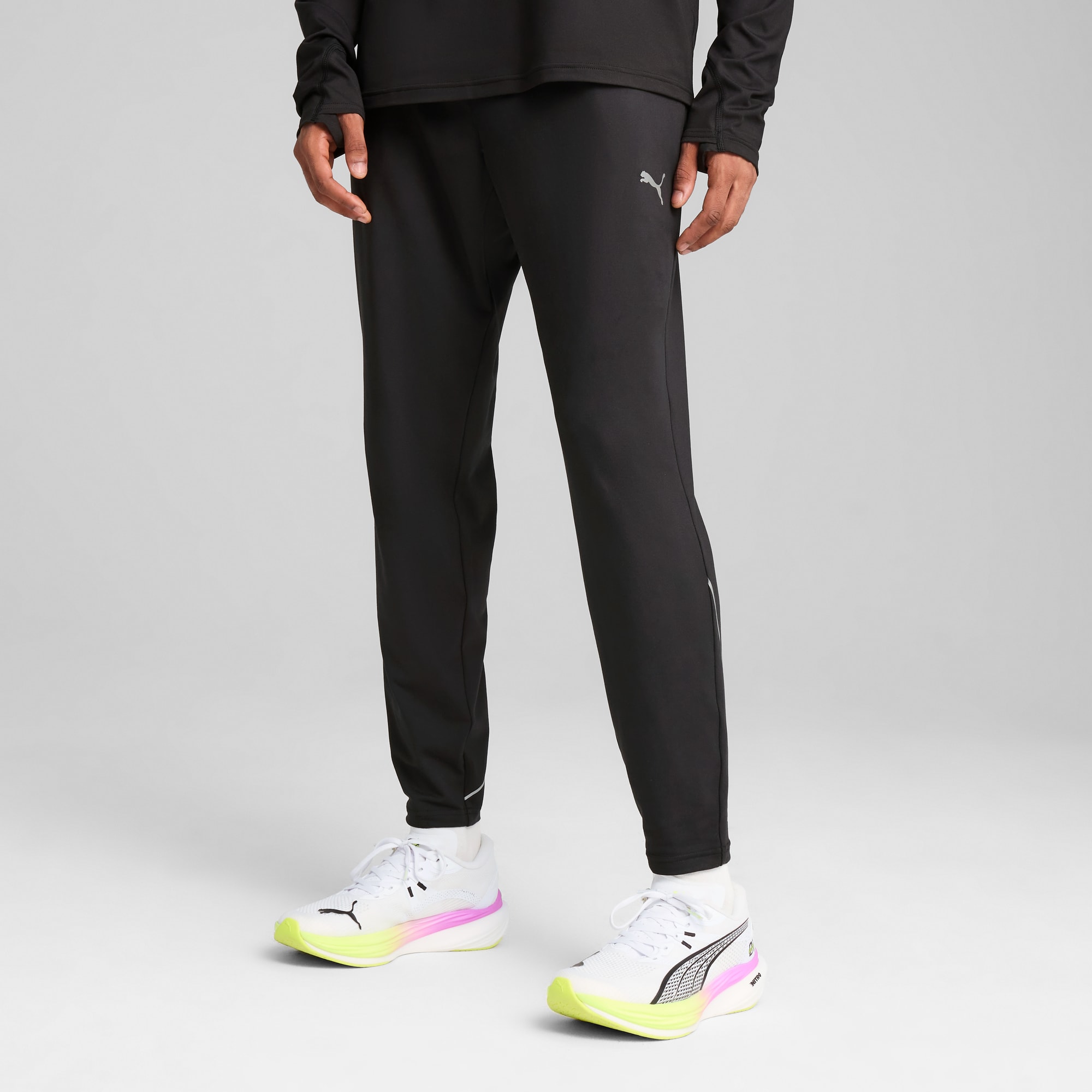 Ein Model in schwarzen Laufhosen und Turnschuhen vor grauem Hintergrund.