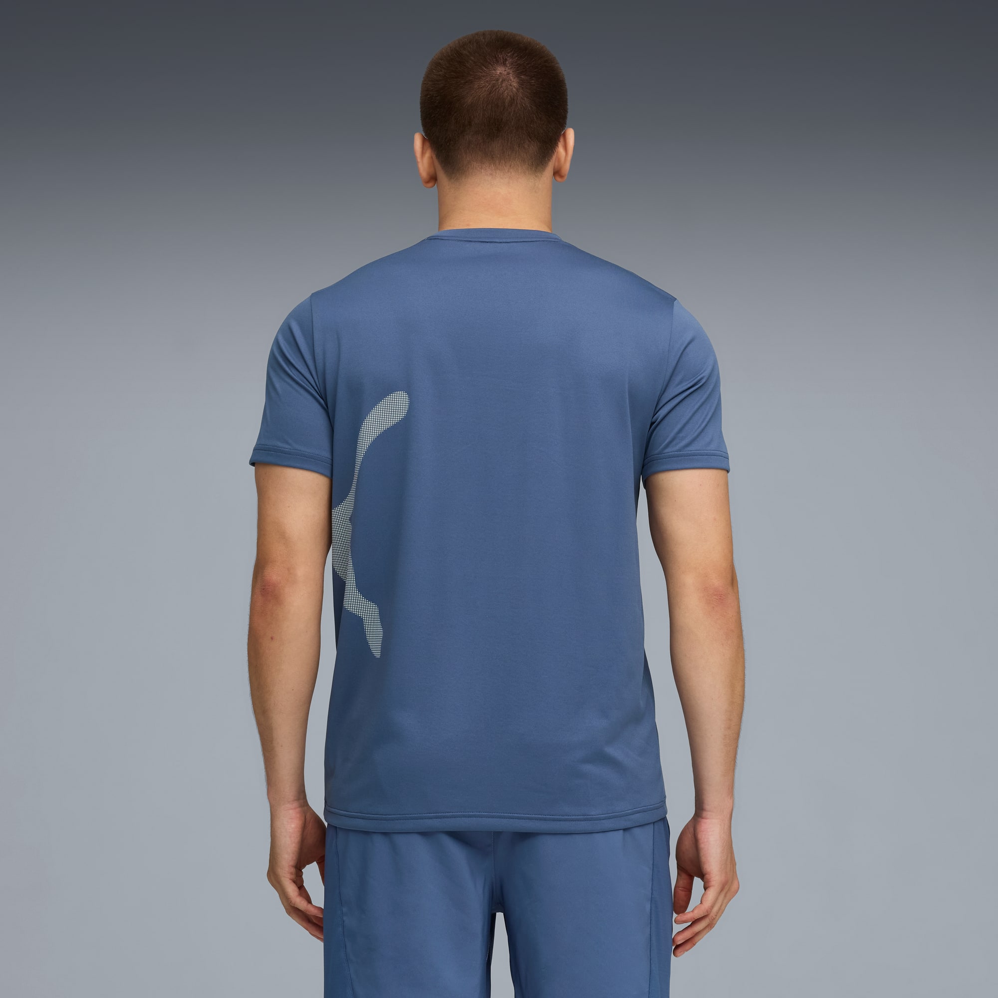 Ein Model mit dem Rücken zum Betrachter vor Grau, trägt blaues T-Shirt, Shorts und Logo.