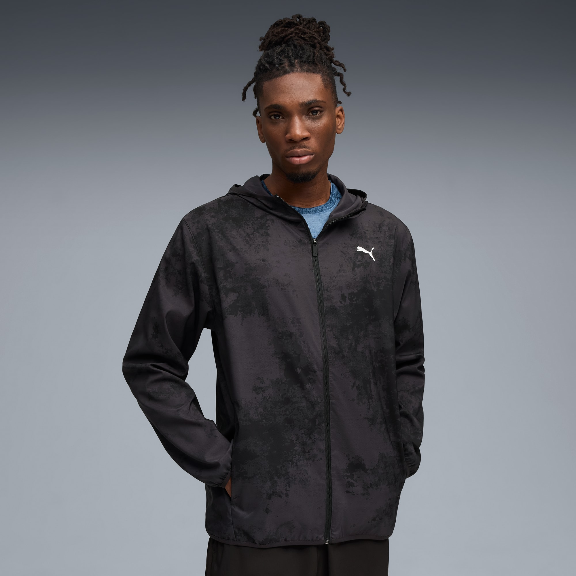 Sur fond gris, un mannequin pose en veste zippée à capuche noire à motifs.