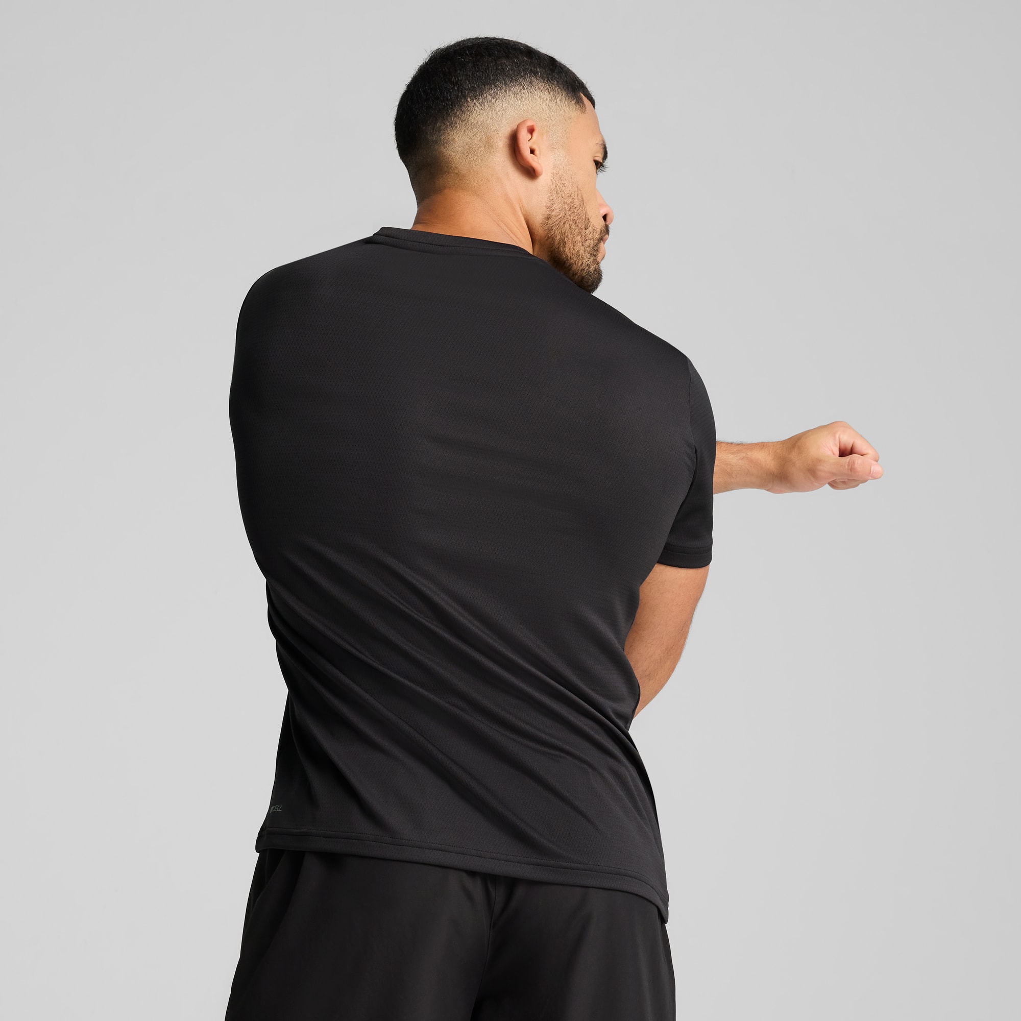 Su sfondo grigio, un modello si allunga in t-shirt e pantaloncini neri.