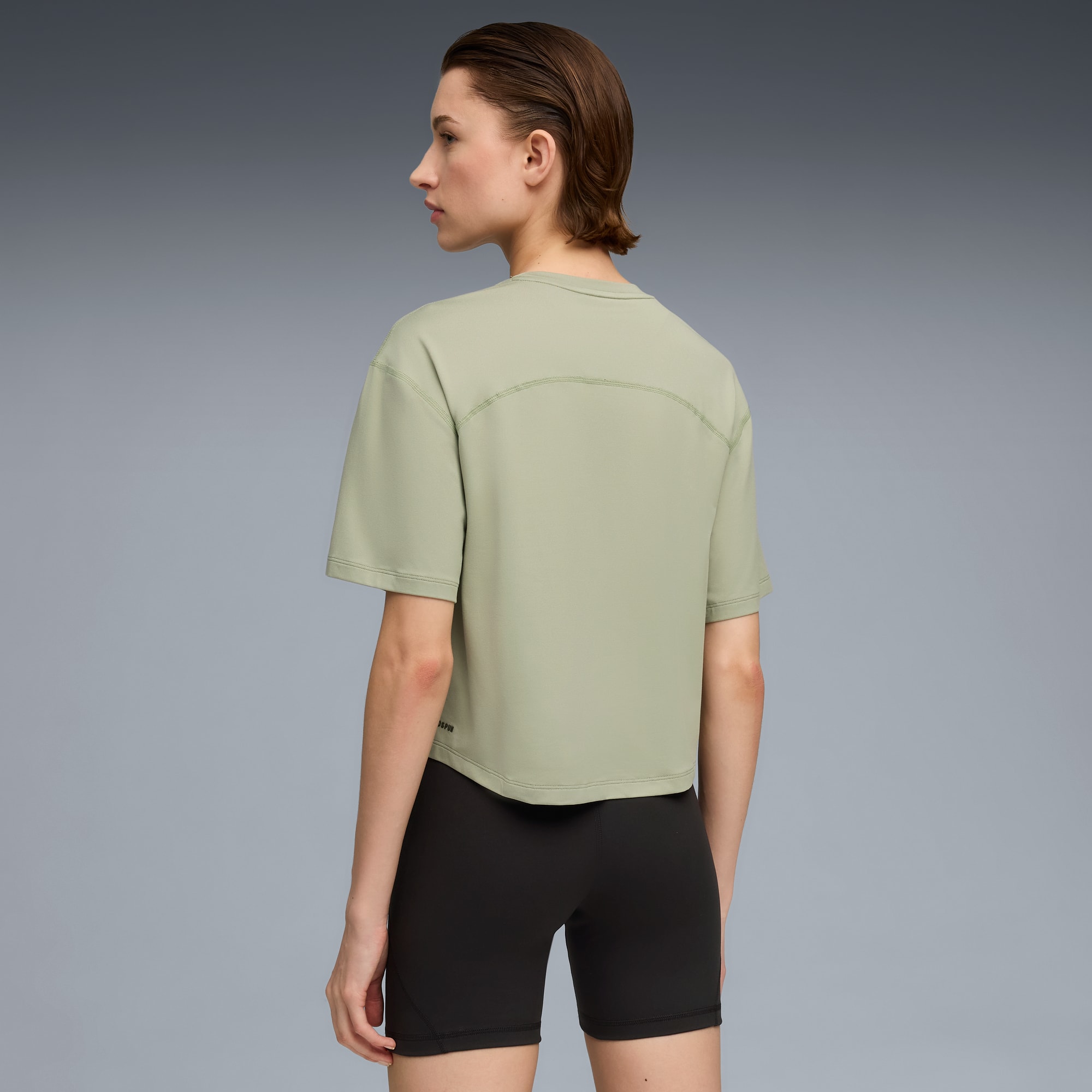 Een model poseert tegen een grijze achtergrond, gekleed in een groen t-shirt en zwarte shorts.