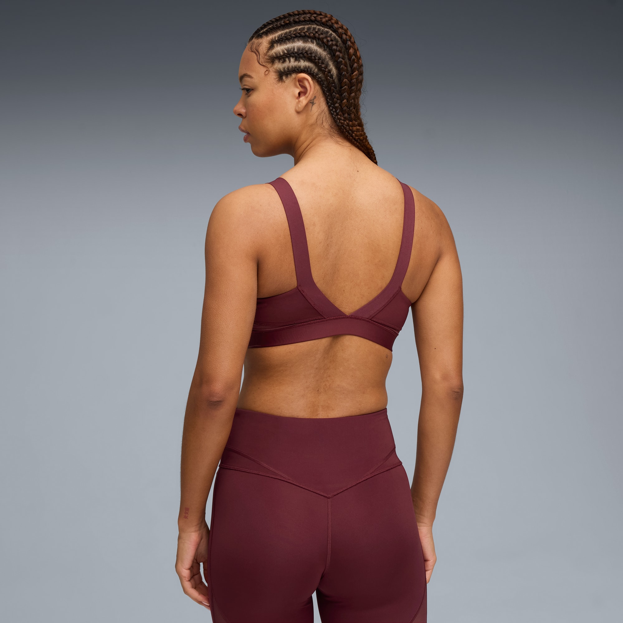 Vor grauem Hintergrund trägt ein Model einen bordeauxroten Sport-BH und Leggings.