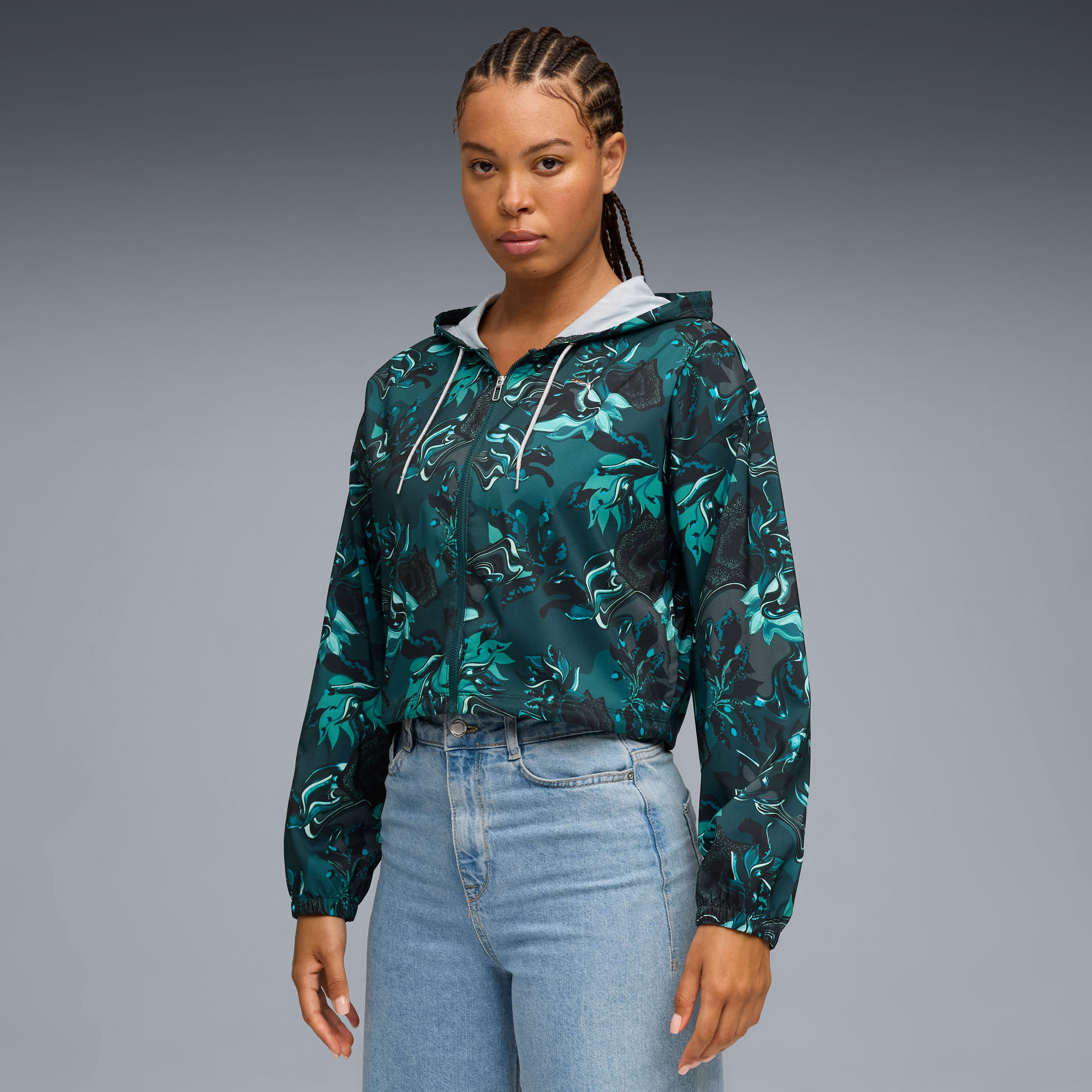 Un modelo posa sobre un fondo gris, vistiendo una chaqueta floral con capucha y vaqueros.