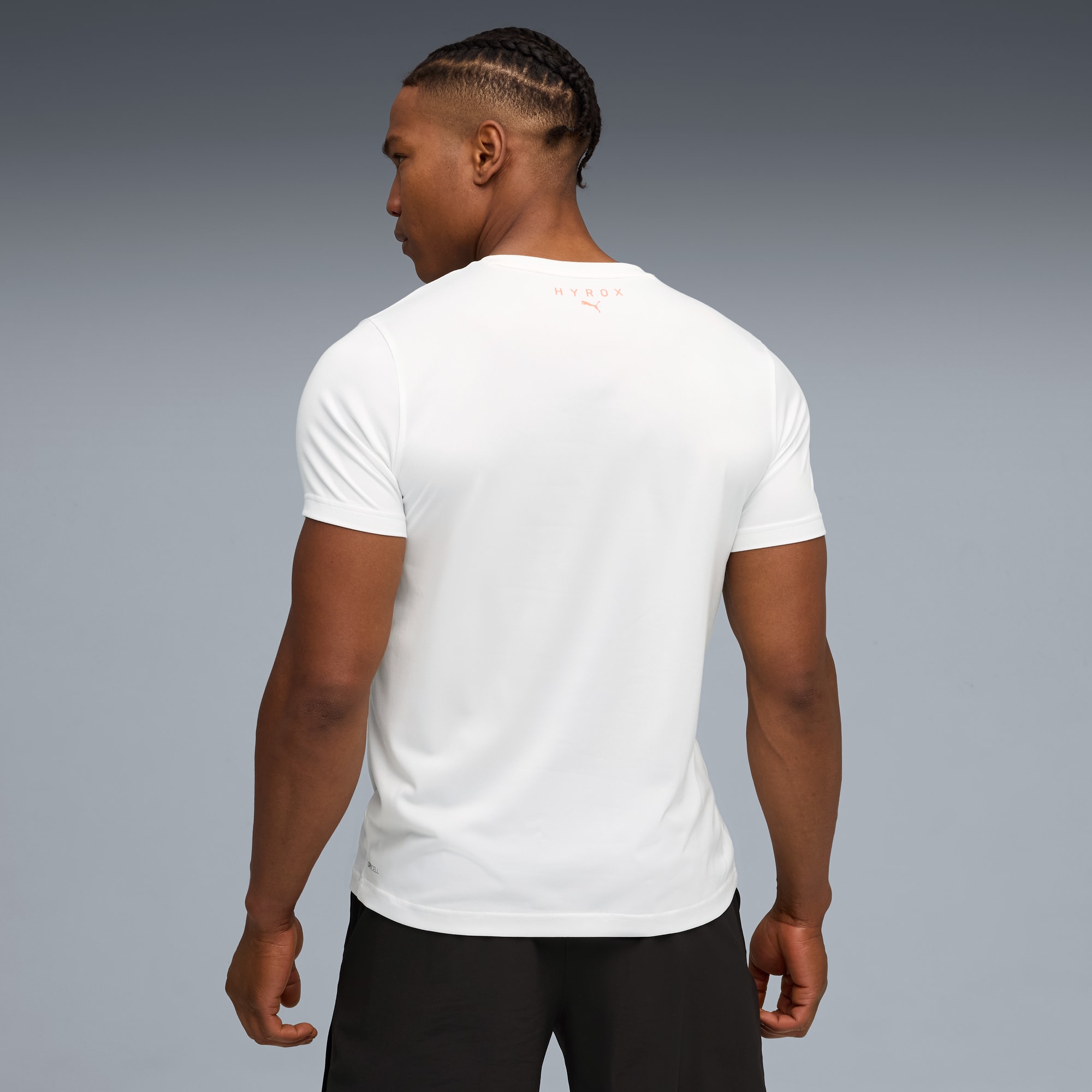 Ein Model vor grauem Hintergrund trägt ein weißes T-Shirt und schwarze Shorts, von hinten.