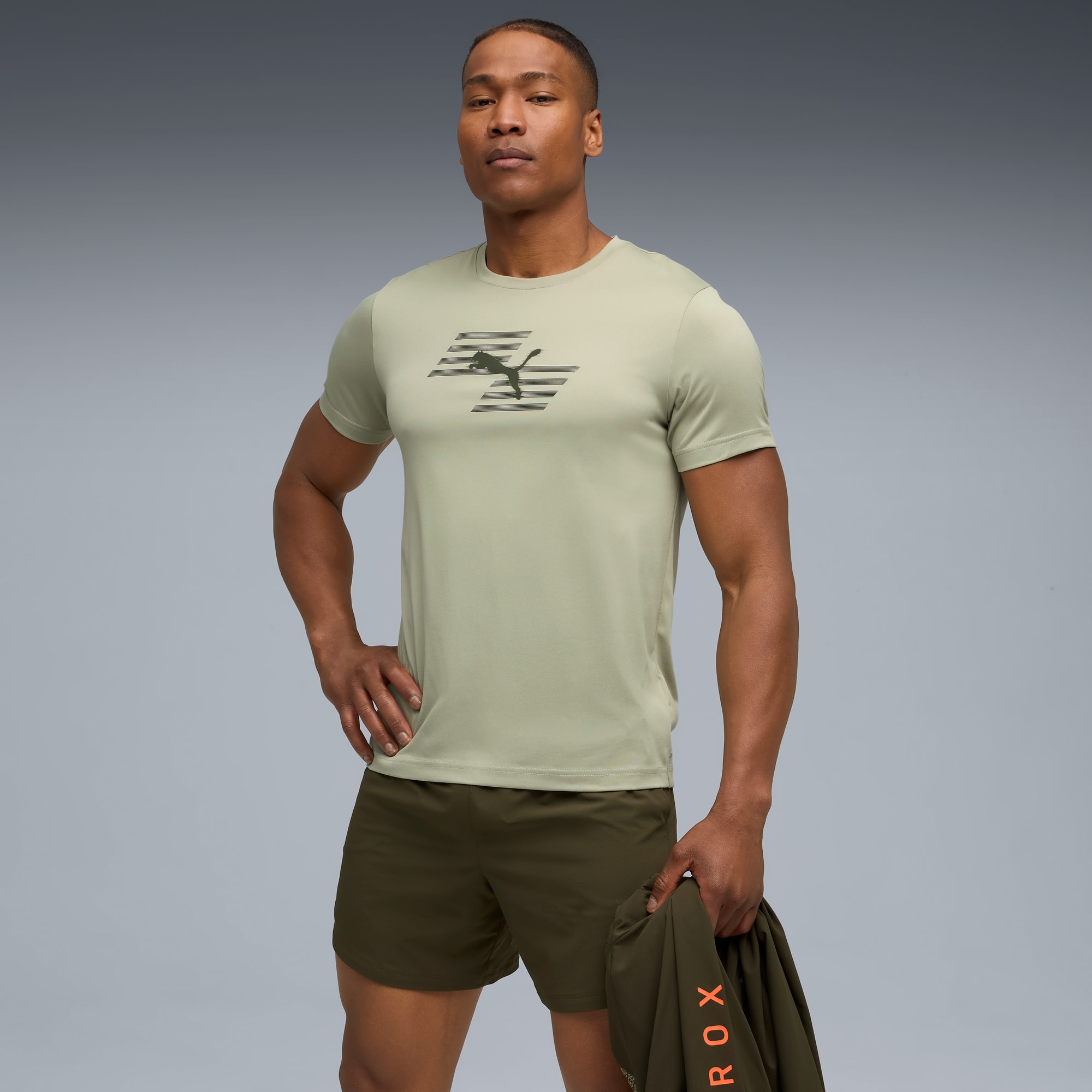 Ein Model posiert vor grauem Hintergrund mit T-Shirt, Shorts und Jacke.