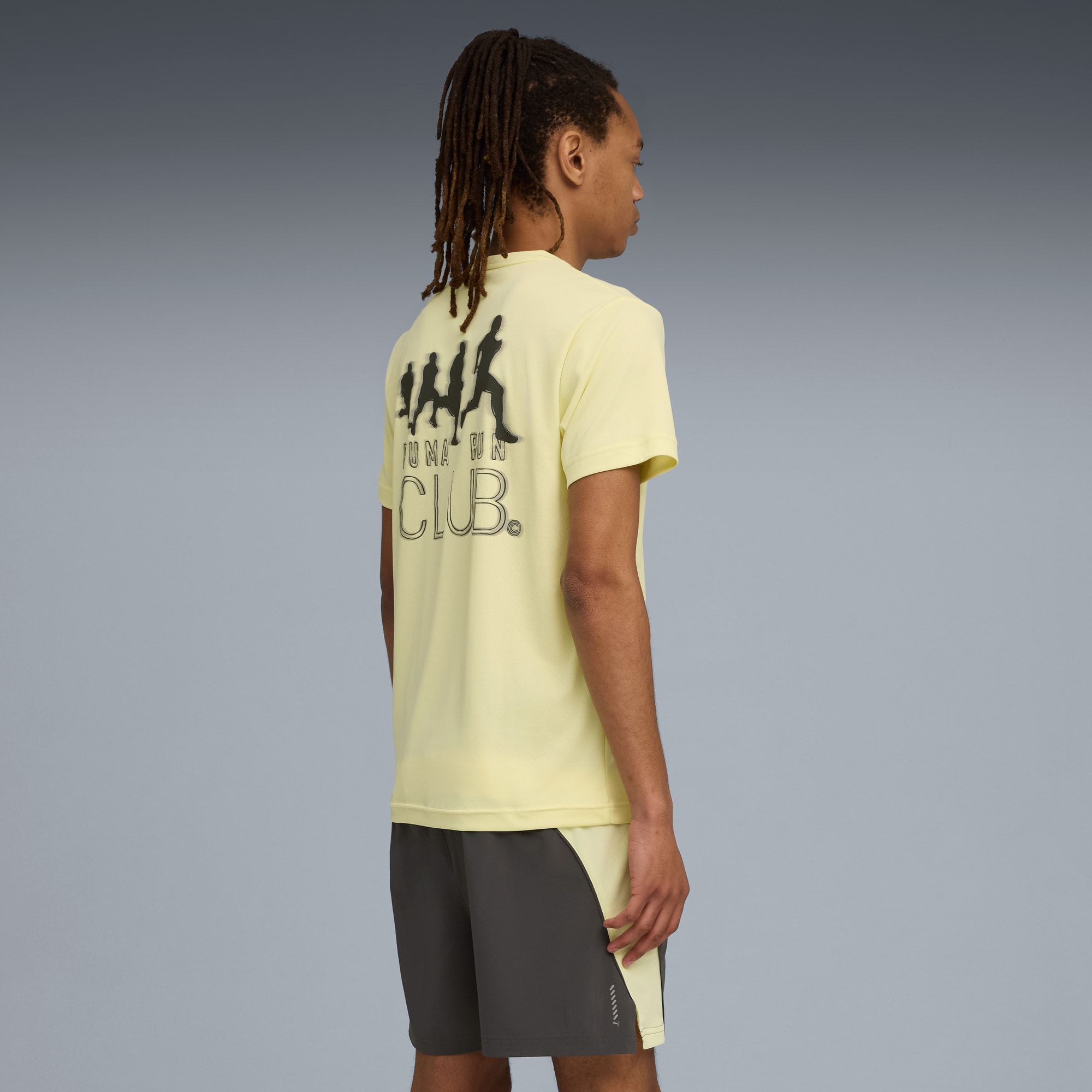 Un modello su sfondo grigio indossa una t-shirt gialla con grafica da corsa e pantaloncini grigi.