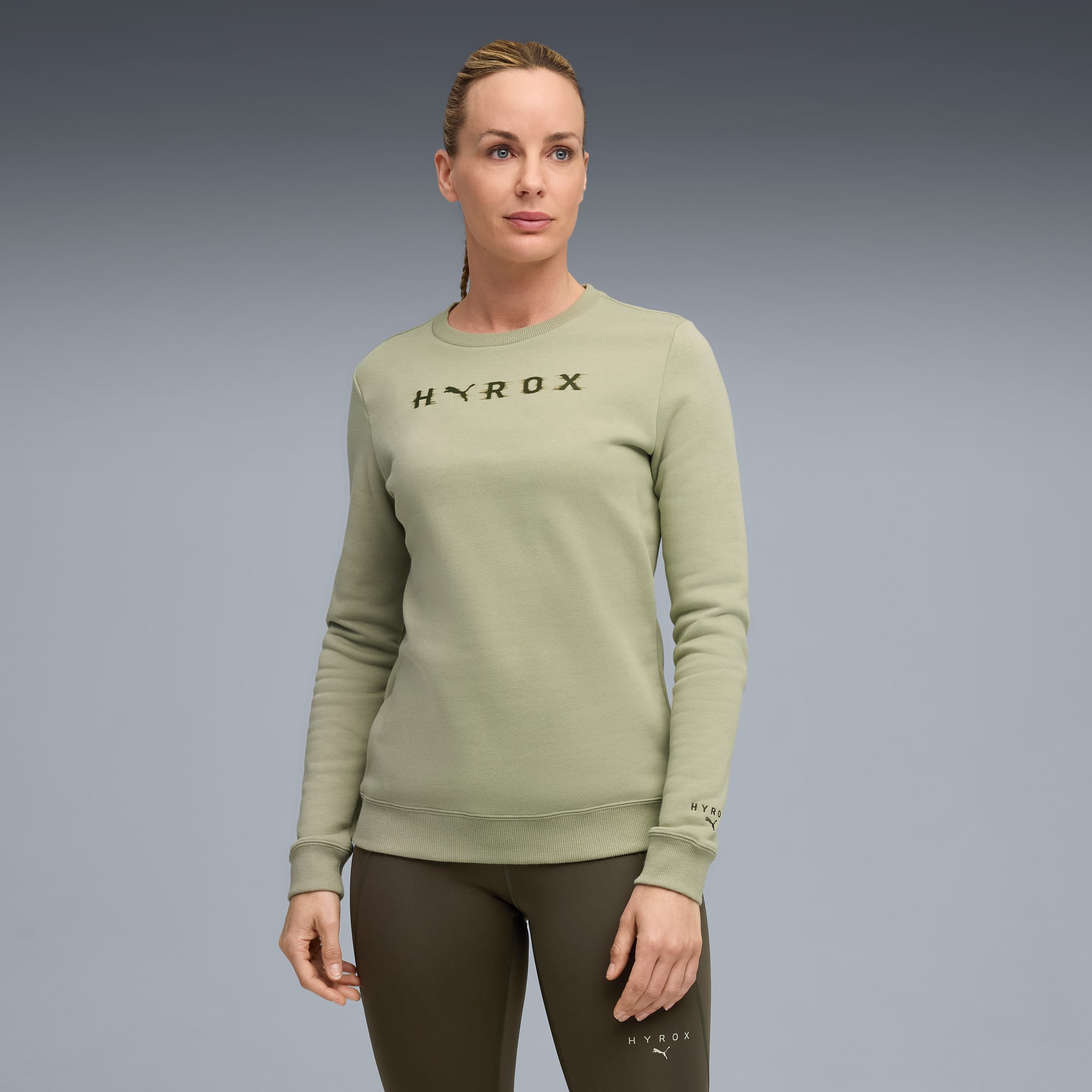 Tegen een grijze achtergrond draagt een model een lichtgroene top en donkergroene legging, kijkend opzij.