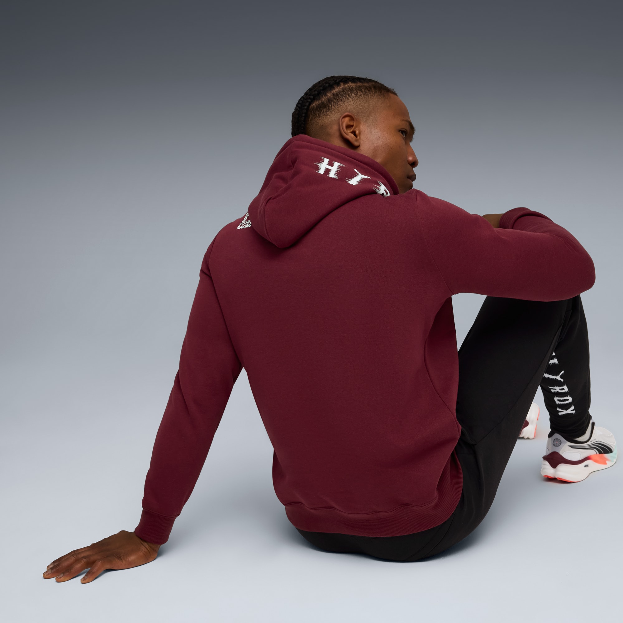 Un mannequin est assis sur un fond gris, portant un sweat à capuche bordeaux et un pantalon de survêtement noir.