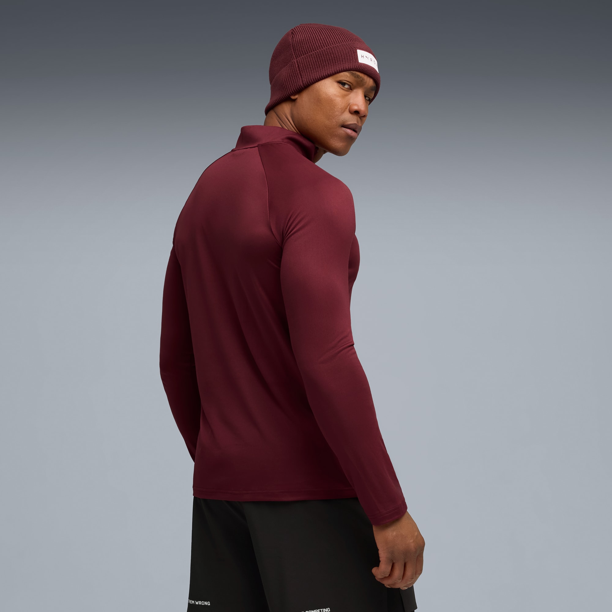 Ein Model blickt über die Schulter, trägt Mütze, Oberteil und Shorts vor Grau.