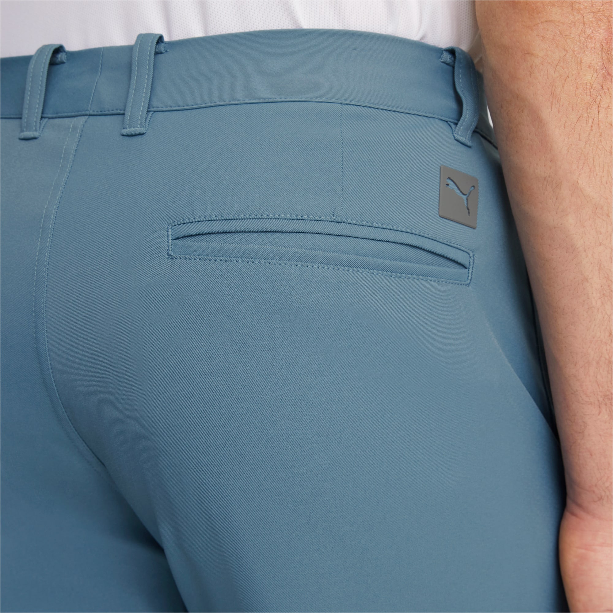 Gros plan sur un pantalon bleu clair avec une poche arrière et un logo gris à la taille.