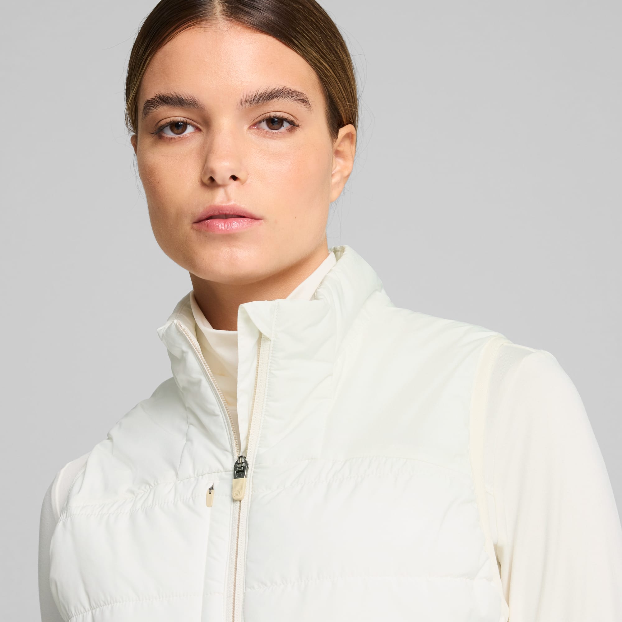 Een model poseert tegen een grijze achtergrond, gekleed in een crèmekleurig gewatteerd vest.