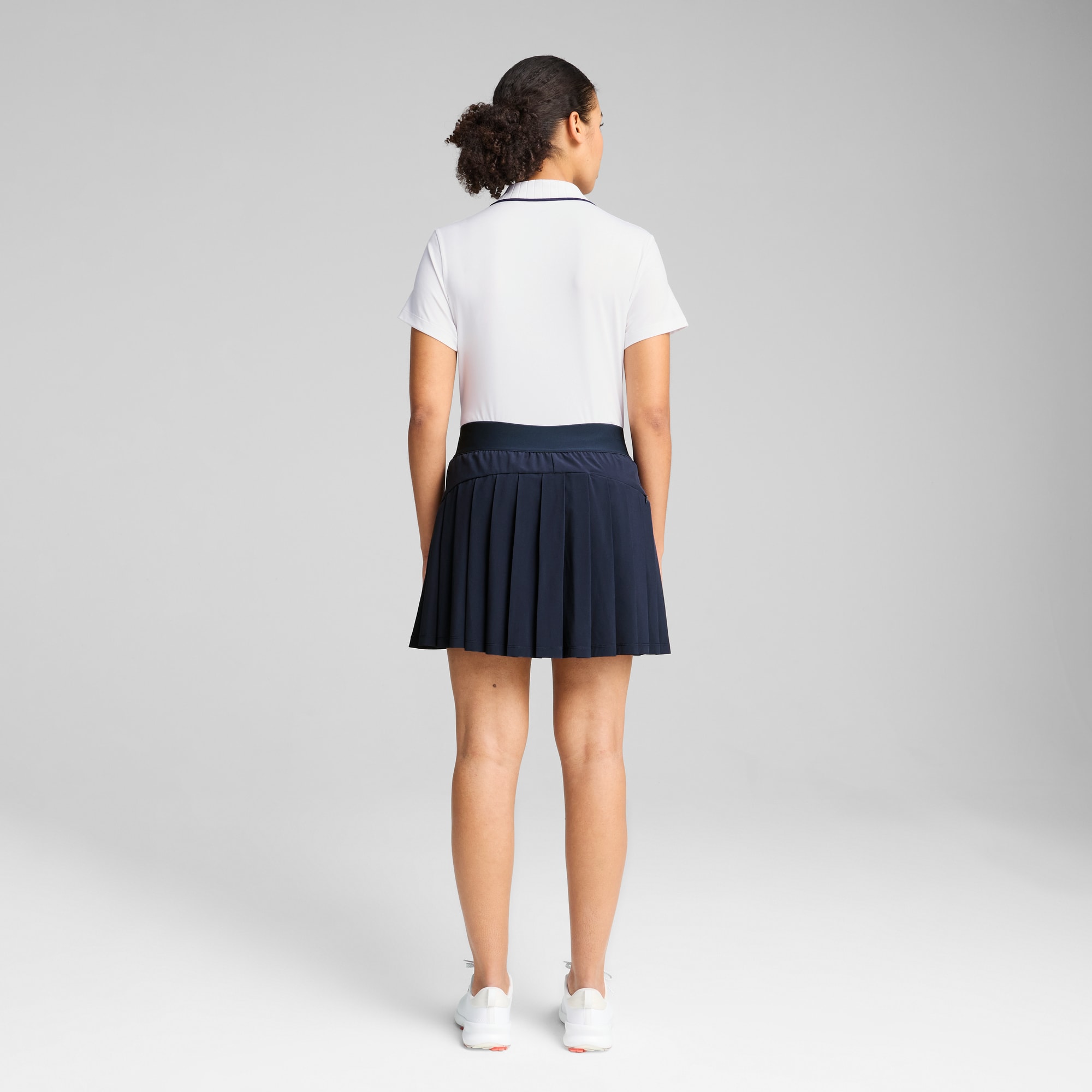 Un mannequin sur fond gris porte un haut blanc, une jupe bleue et des baskets.