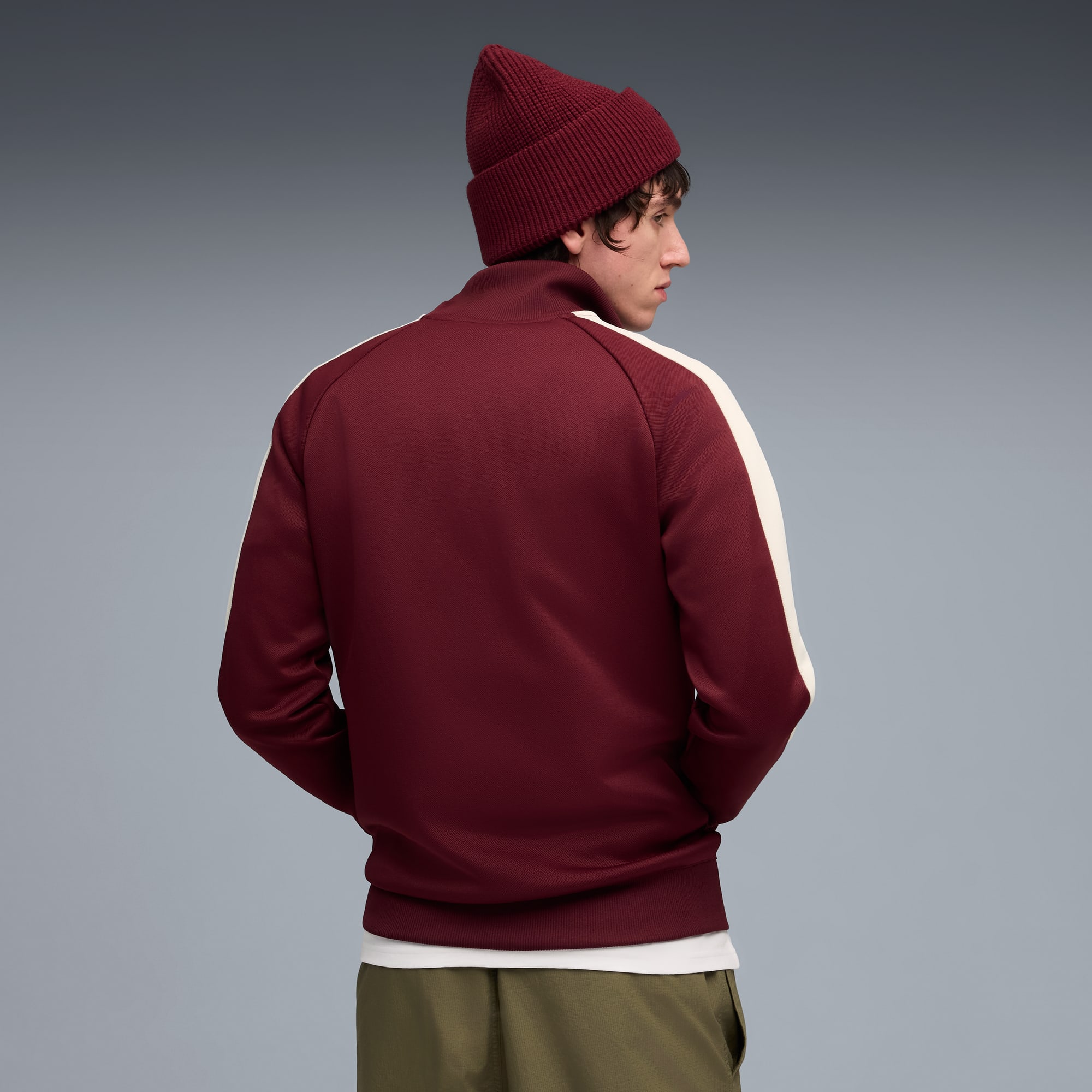 Un mannequin portant une veste bordeaux et un bonnet sur fond gris, regardant sur le côté.