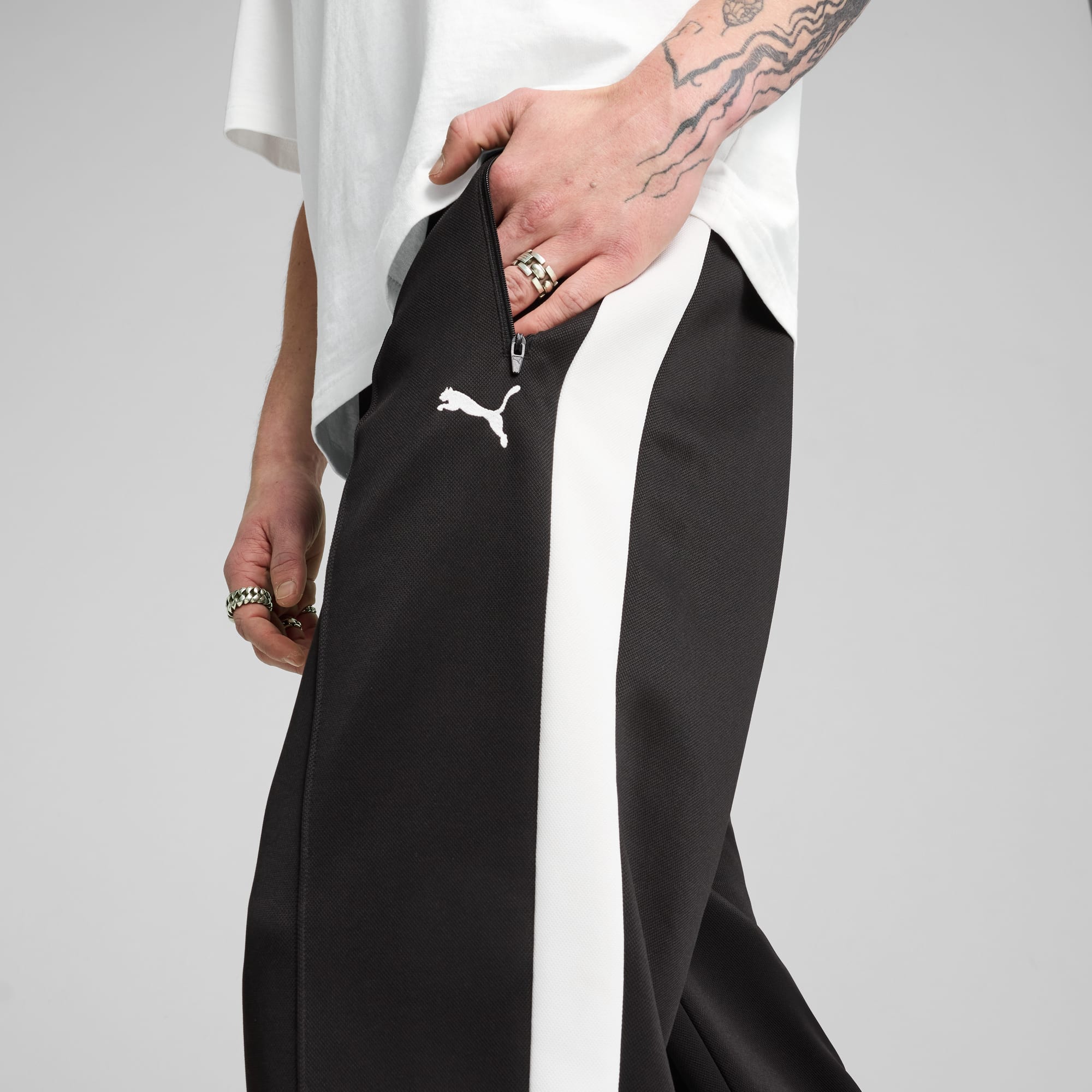 Un modello indossa pantaloni neri con una striscia bianca su sfondo grigio.