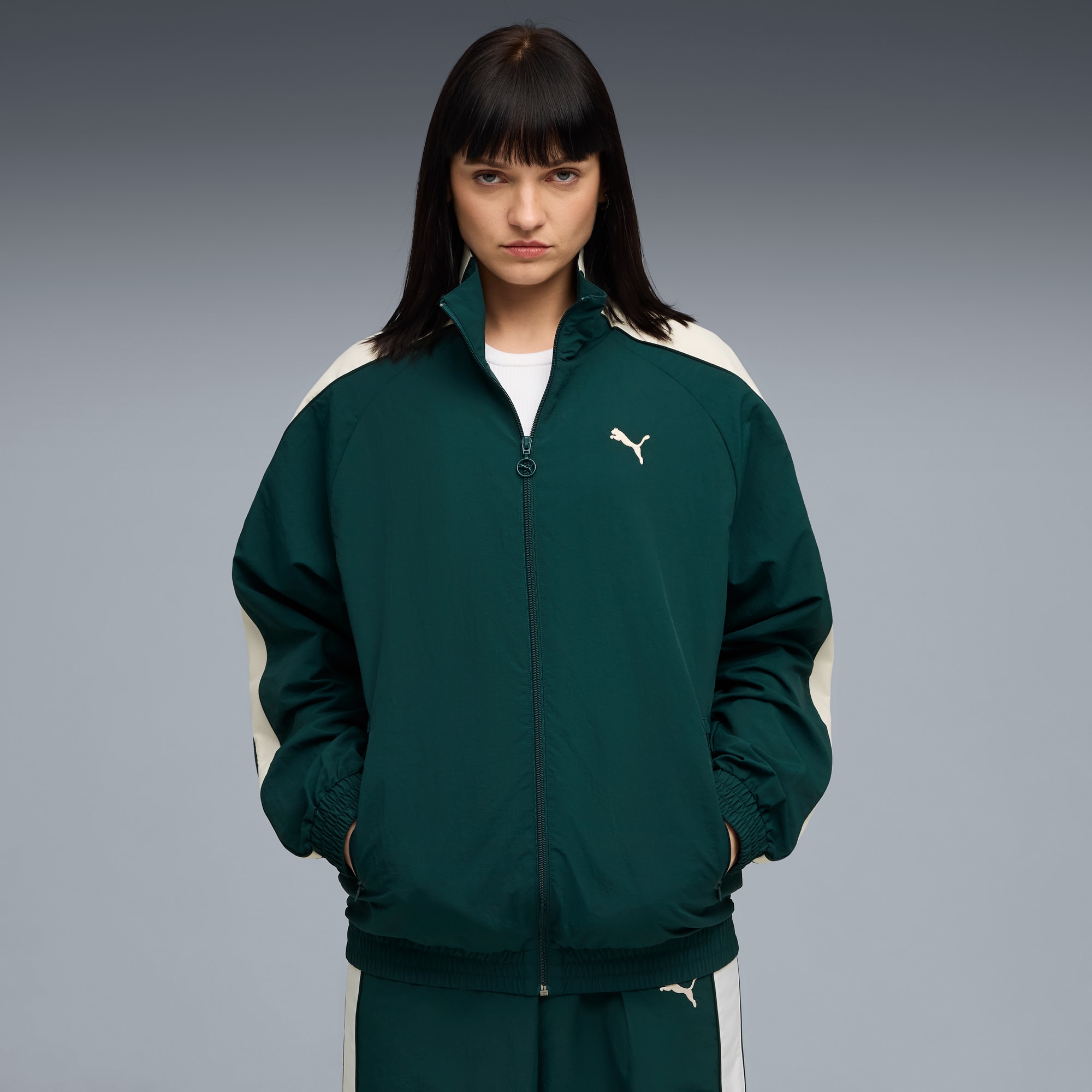 Ein Model posiert vor grauem Hintergrund und trägt eine grün-weiße Puma-Jacke.