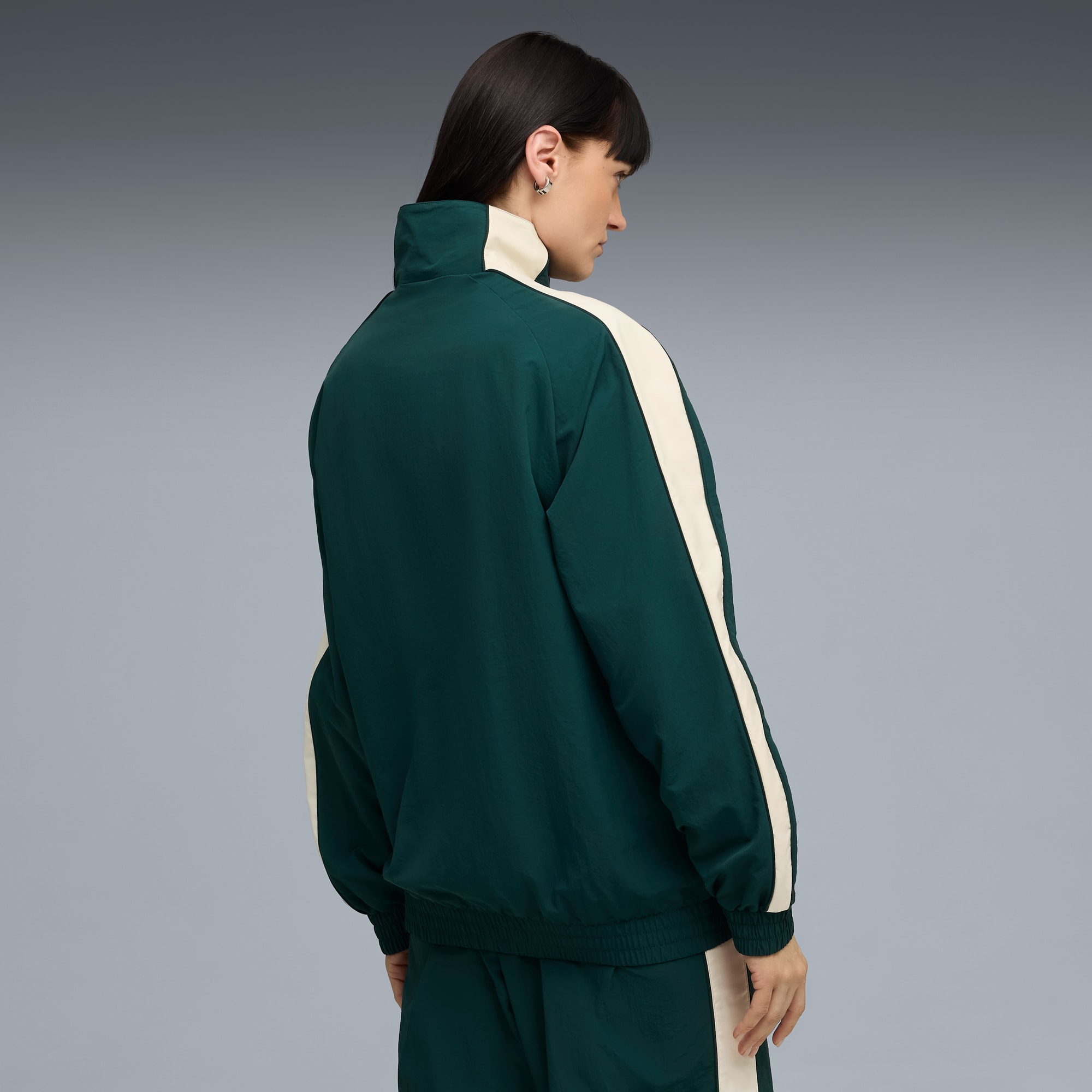 Ein Model mit dem Rücken zu uns vor grauem Hintergrund, trägt eine grün-weiße Jacke.