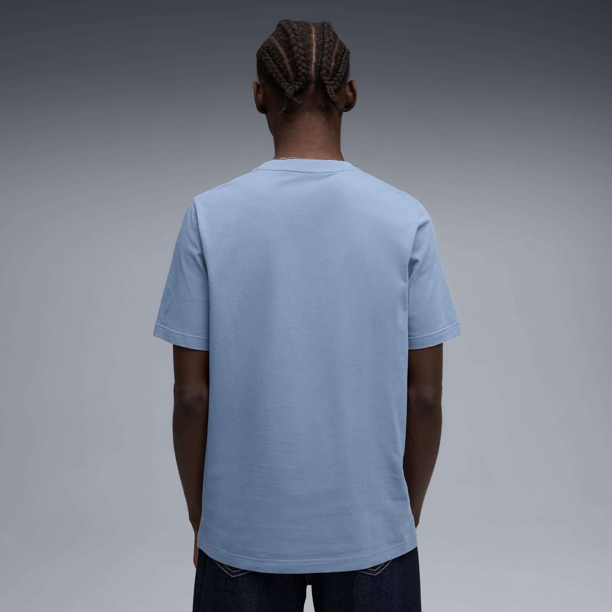 Een model staat met de rug naar de camera, draagt een blauw T-shirt en jeans.