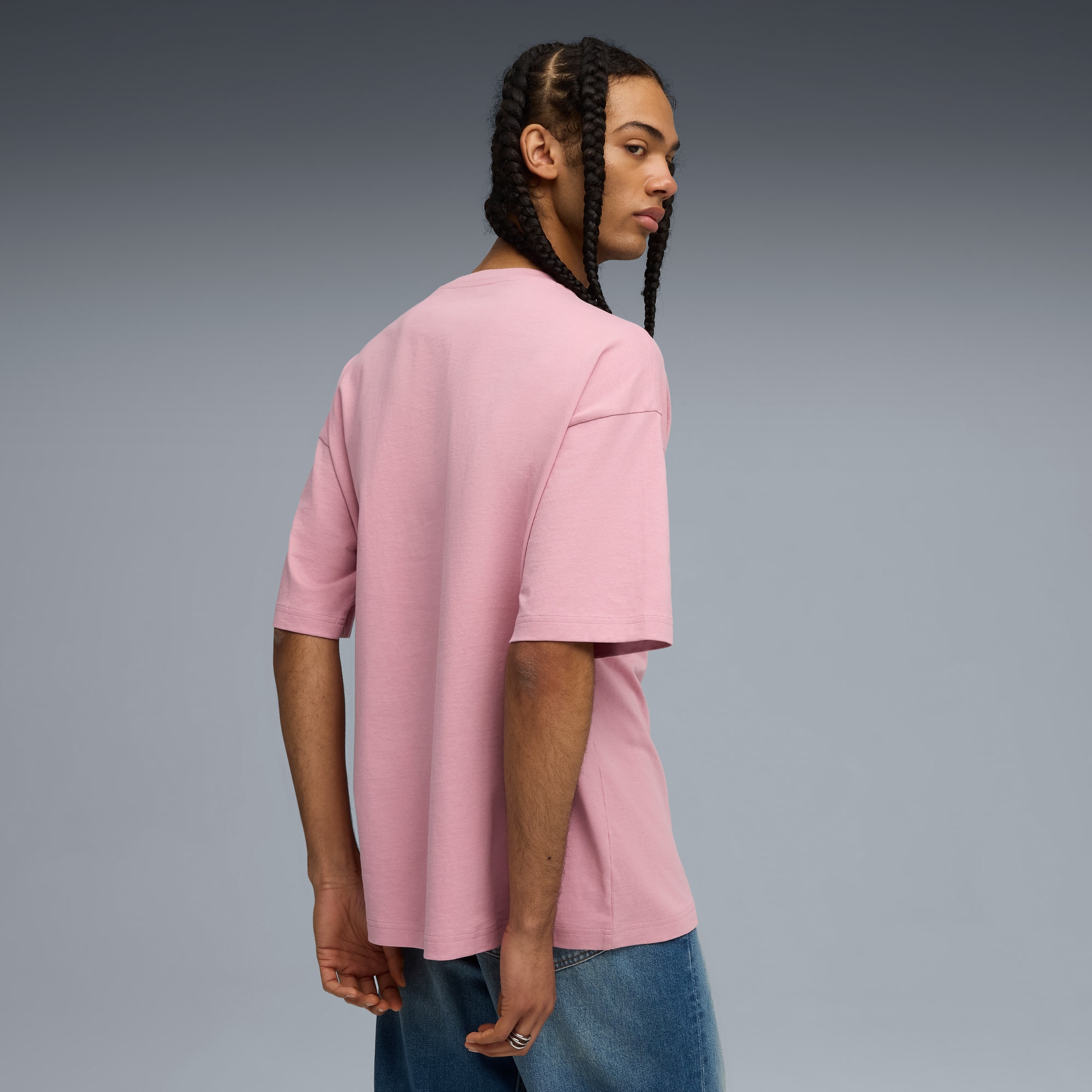 Un modello con trecce guarda indietro con una t-shirt rosa e jeans.