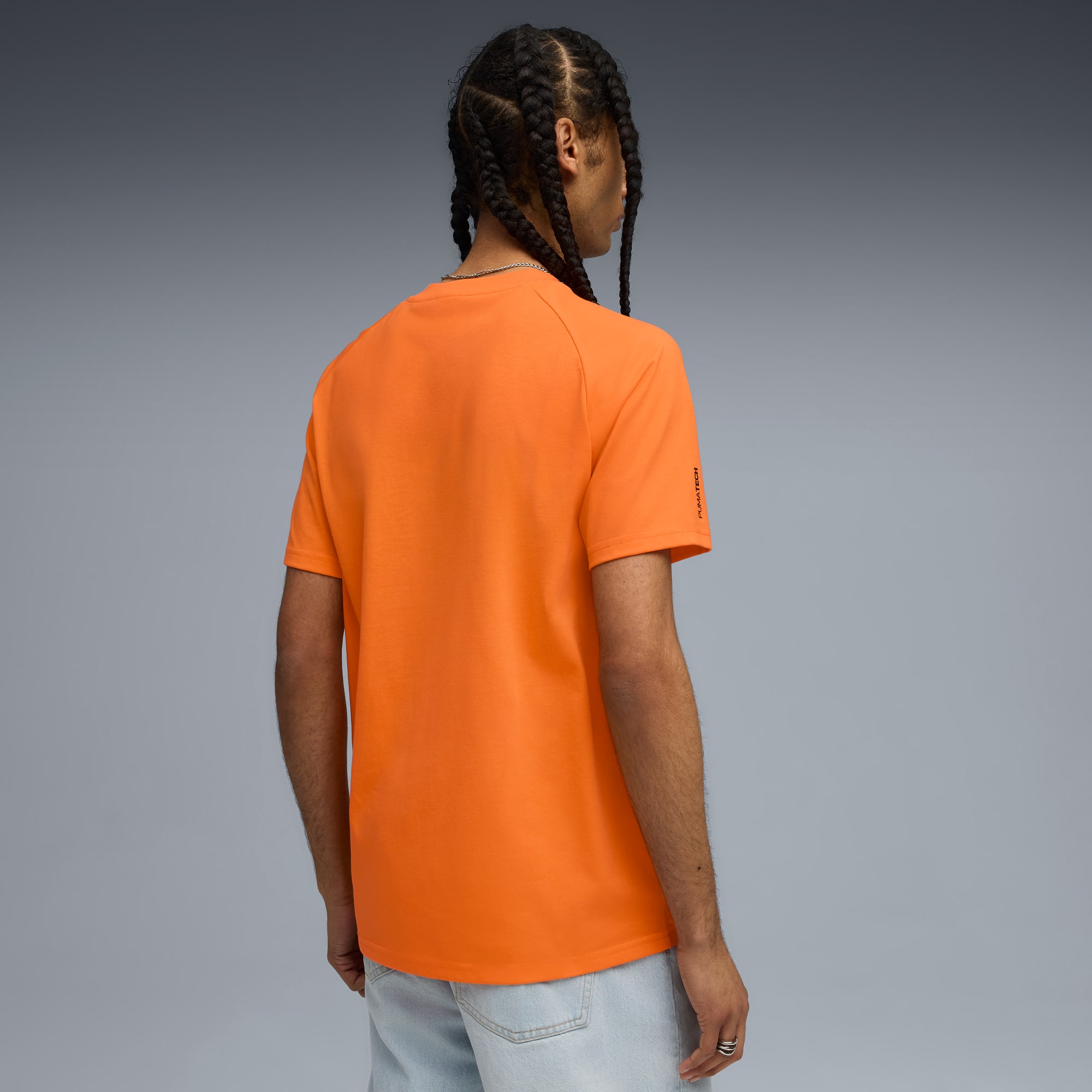Un modèle de dos sur fond gris, portant un t-shirt orange et un short en jean clair.