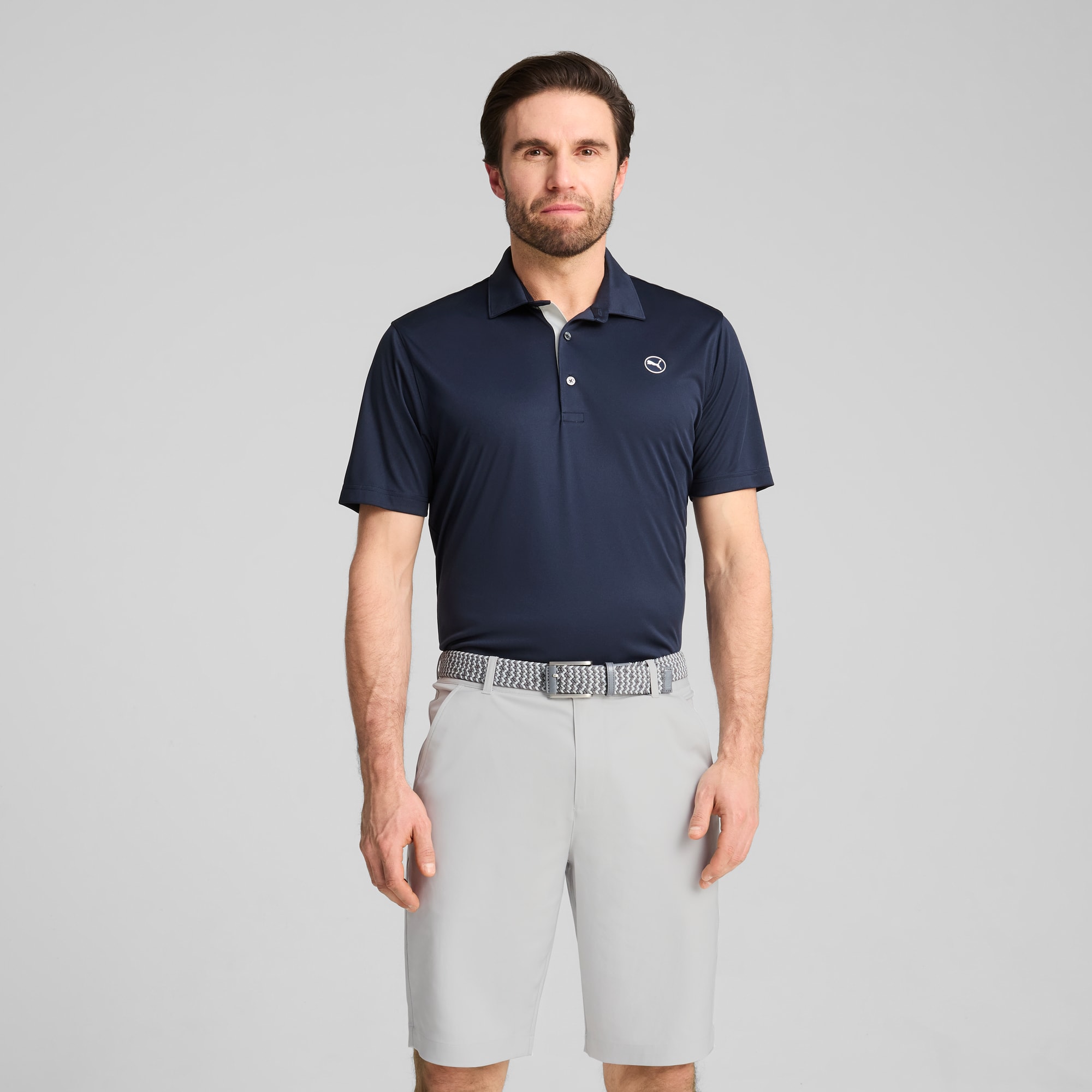 Een model poseert tegen een grijze achtergrond, gekleed in een marineblauwe polo en grijze korte broek.