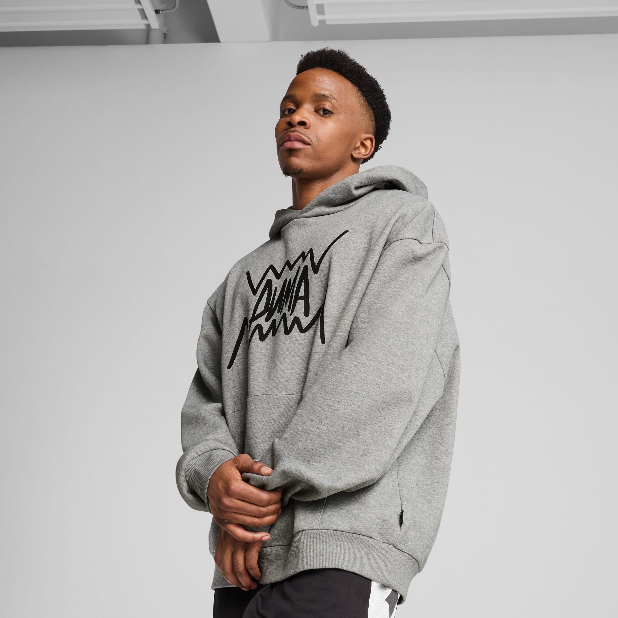 Un modèle pose sur fond gris, portant un sweat à capuche gris avec un logo noir.