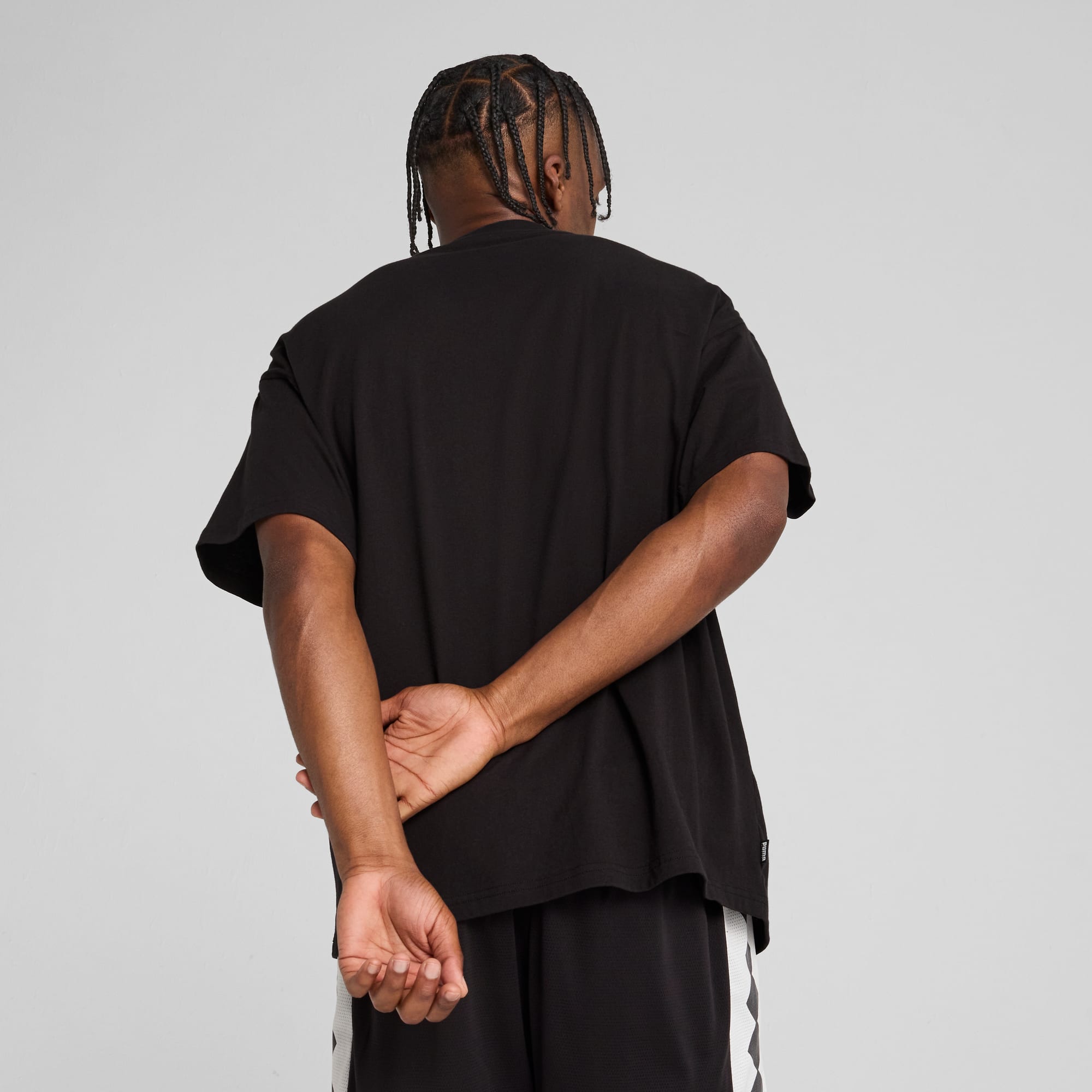 A model faces away against grey, wearing a black t-shirt and black shorts.