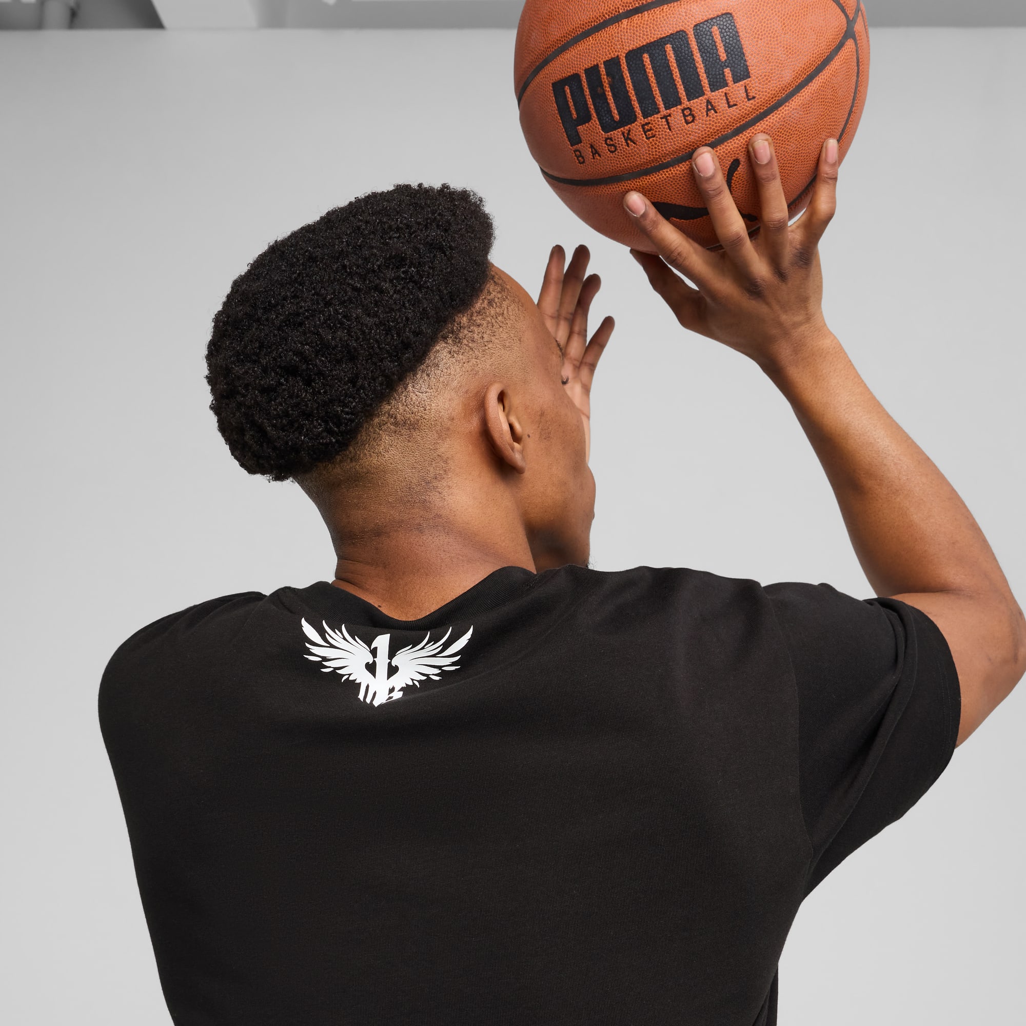 Un modèle de dos sur fond gris, tenant un ballon de basket Puma en t-shirt noir.