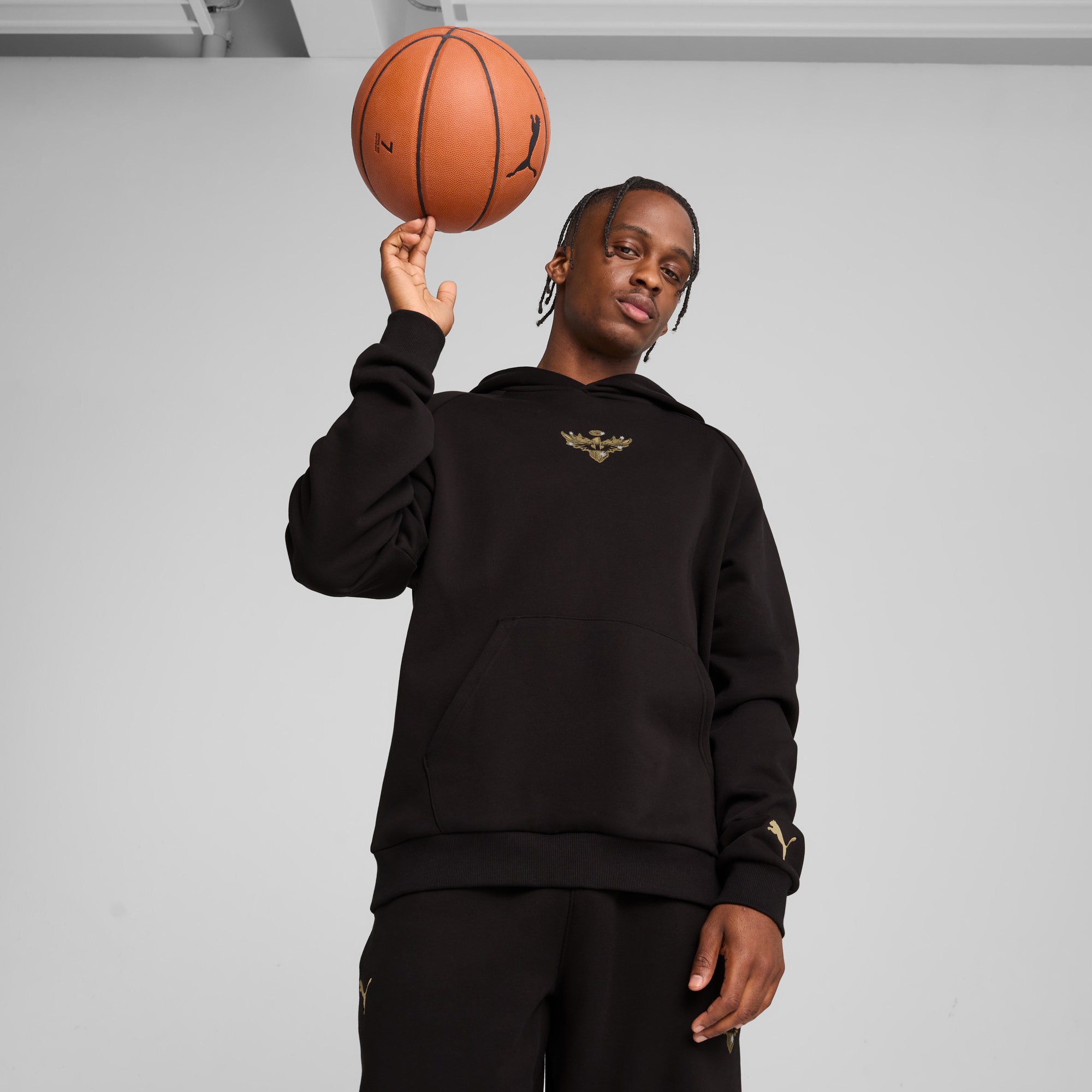 Vor grauem Hintergrund balanciert ein Model einen Basketball auf einem Finger, mit schwarzem Hoodie.