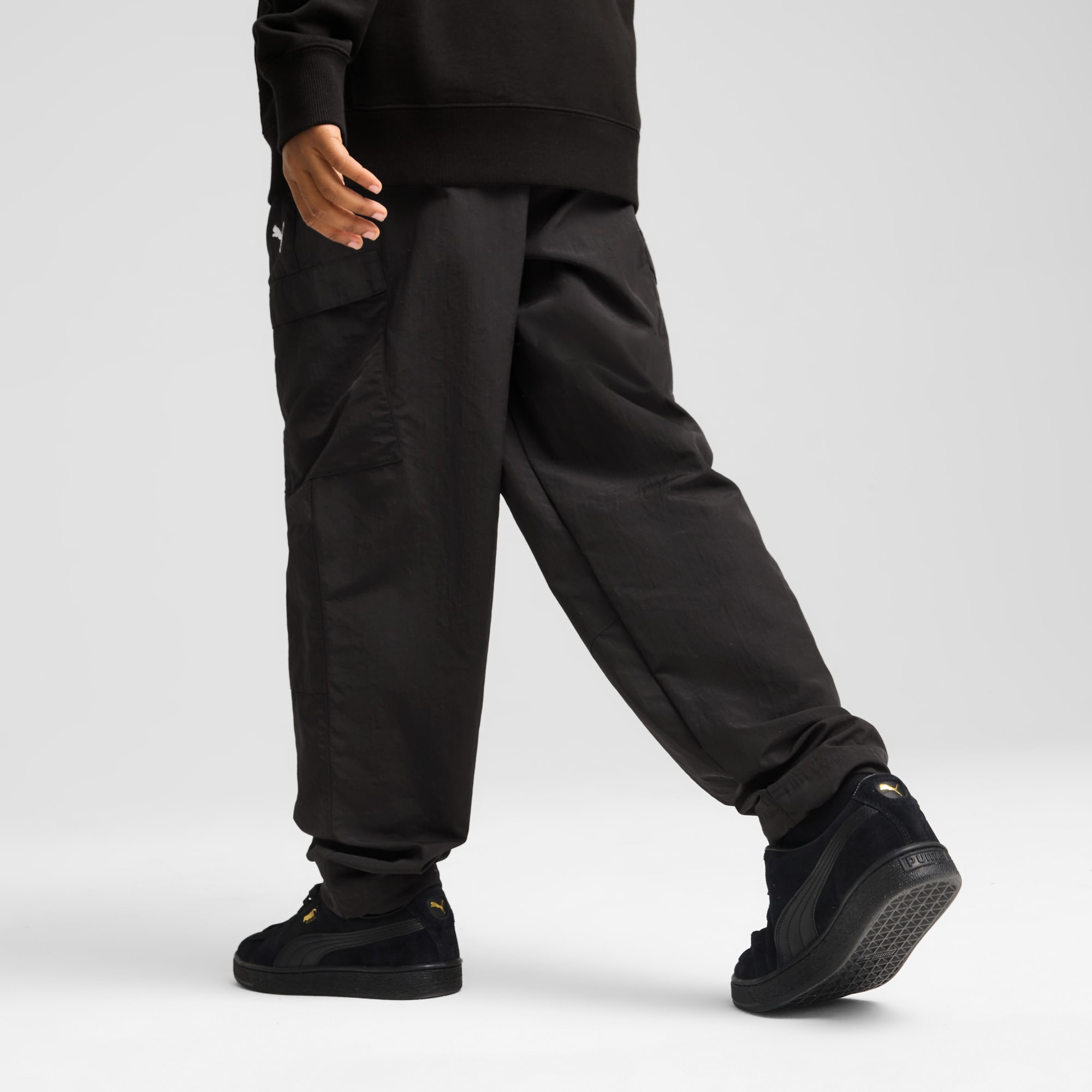 Tegen een grijze achtergrond loopt een model in een zwarte broek en bijpassende sneakers.