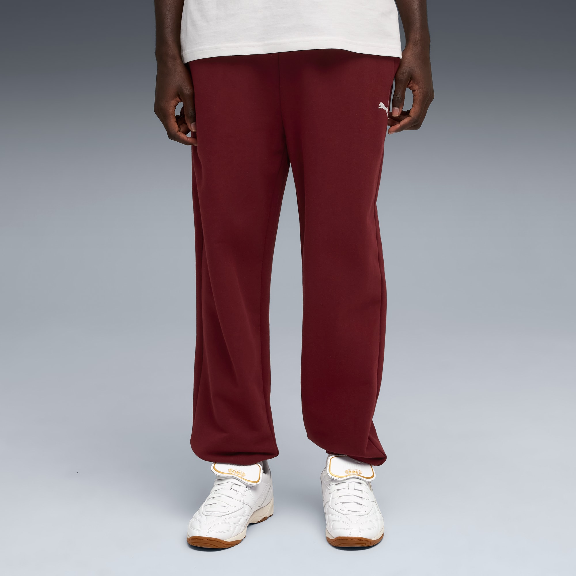 Un modello in piedi su sfondo grigio indossa t-shirt bianca, pantaloni rossi e scarpe da ginnastica.