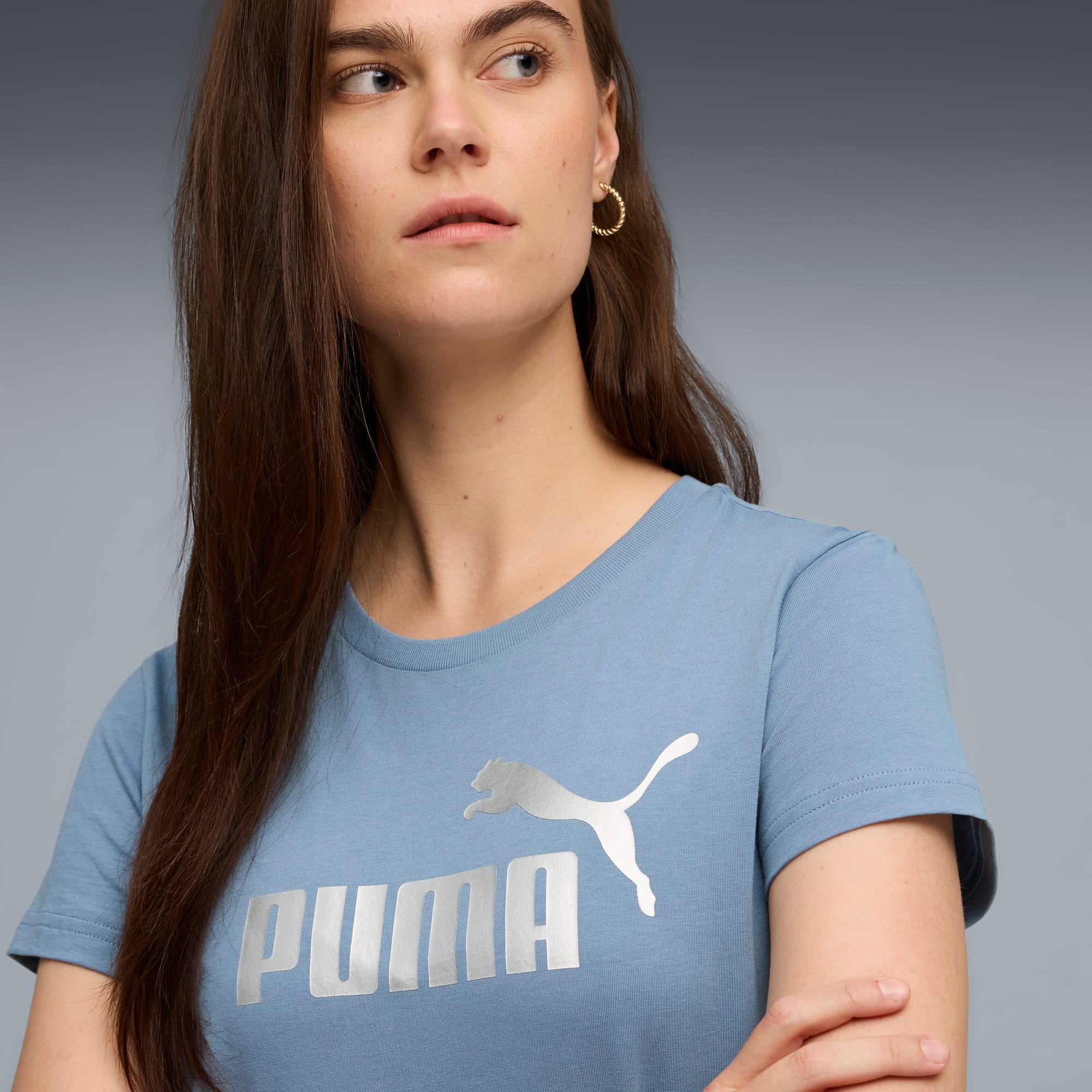 Una modella posa su sfondo grigio, indossando una t-shirt Puma blu.
