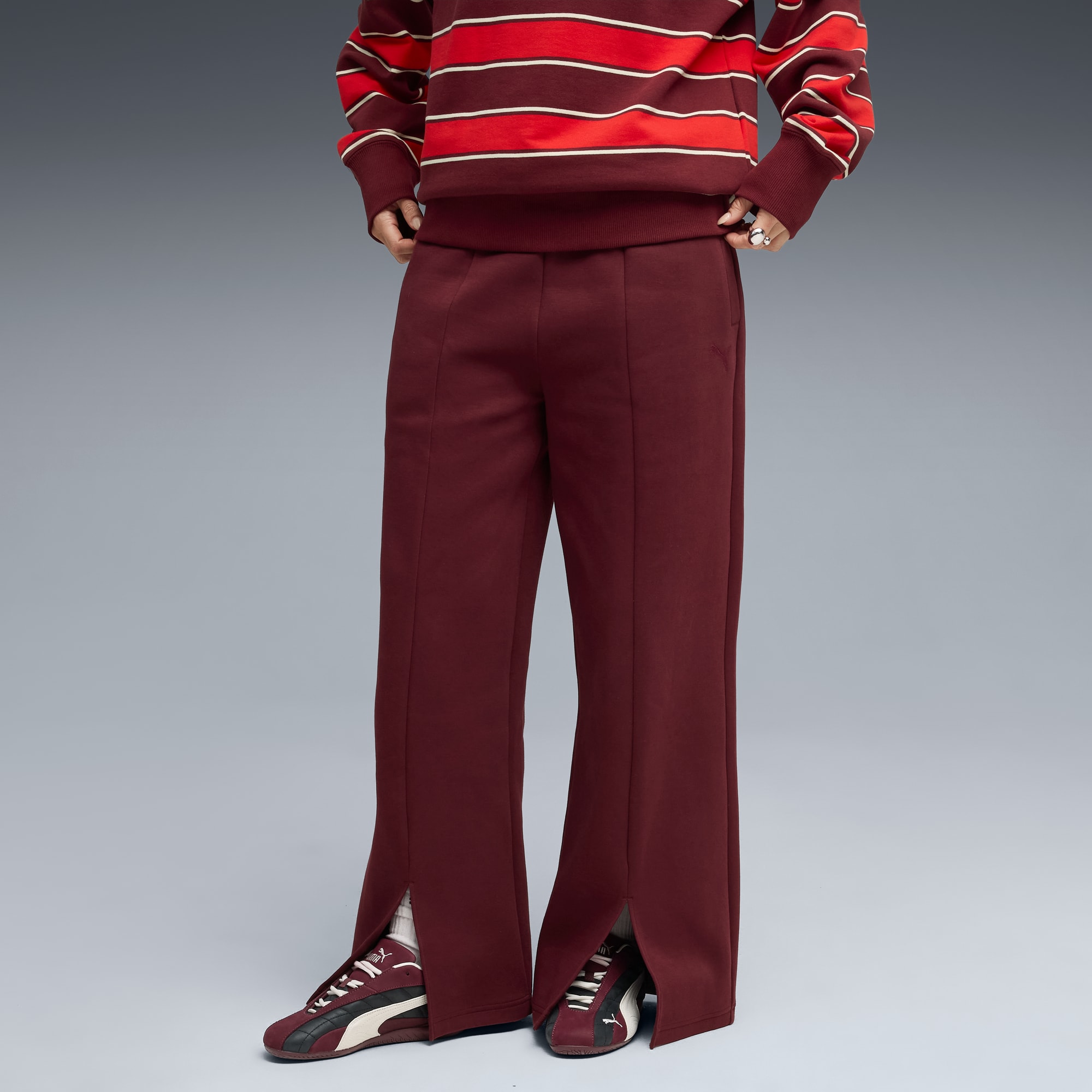 Un mannequin porte un haut rayé, un pantalon bordeaux fendu et des baskets sur fond gris.