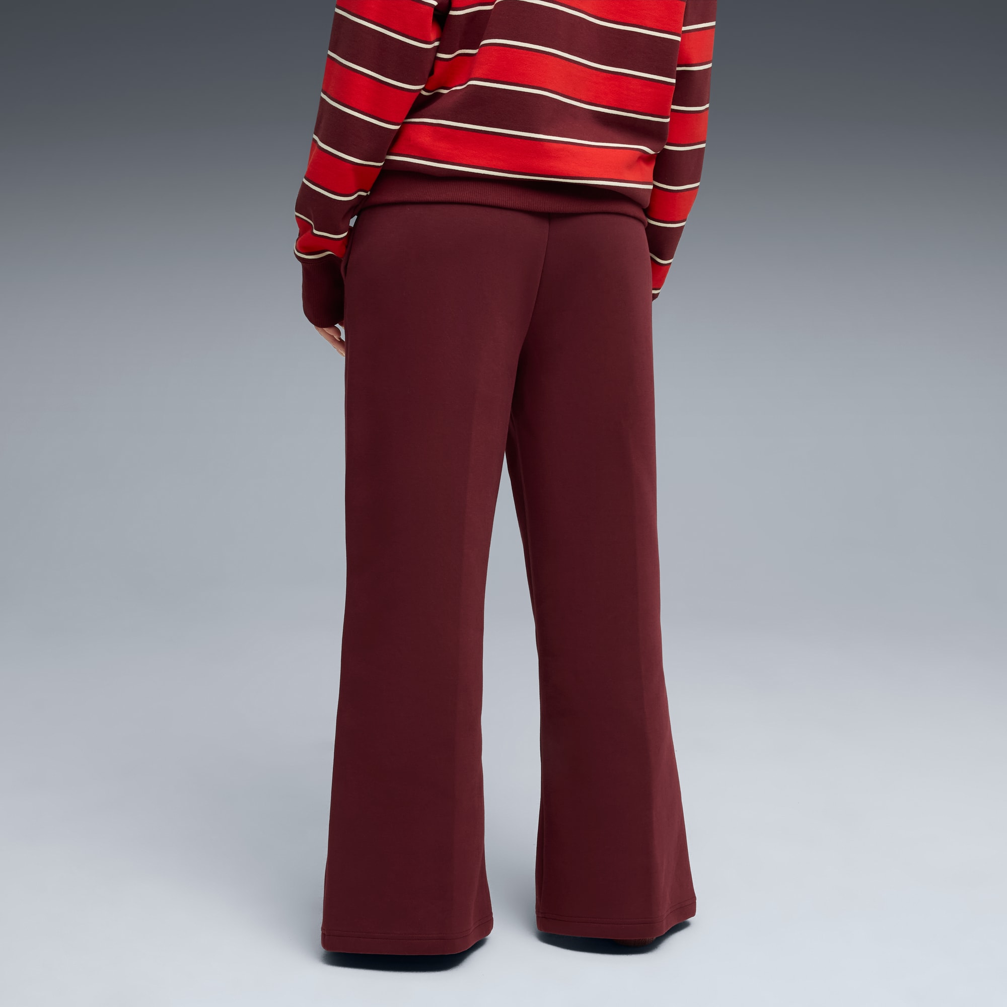 Sur fond gris, un mannequin de dos porte un haut rayé et un pantalon ample bordeaux.