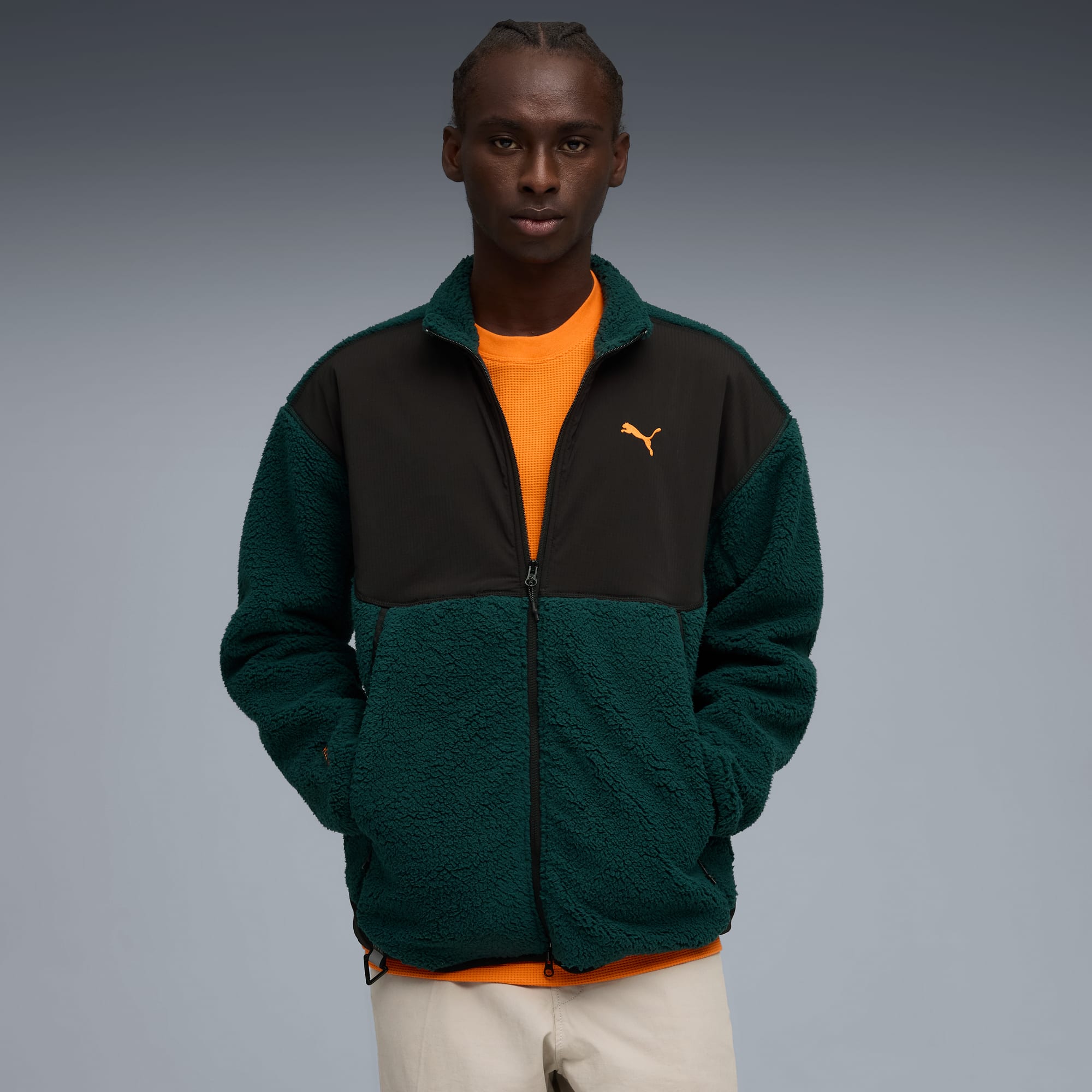 Een model poseert tegen grijs, in een zwart-groen jack en oranje shirt.