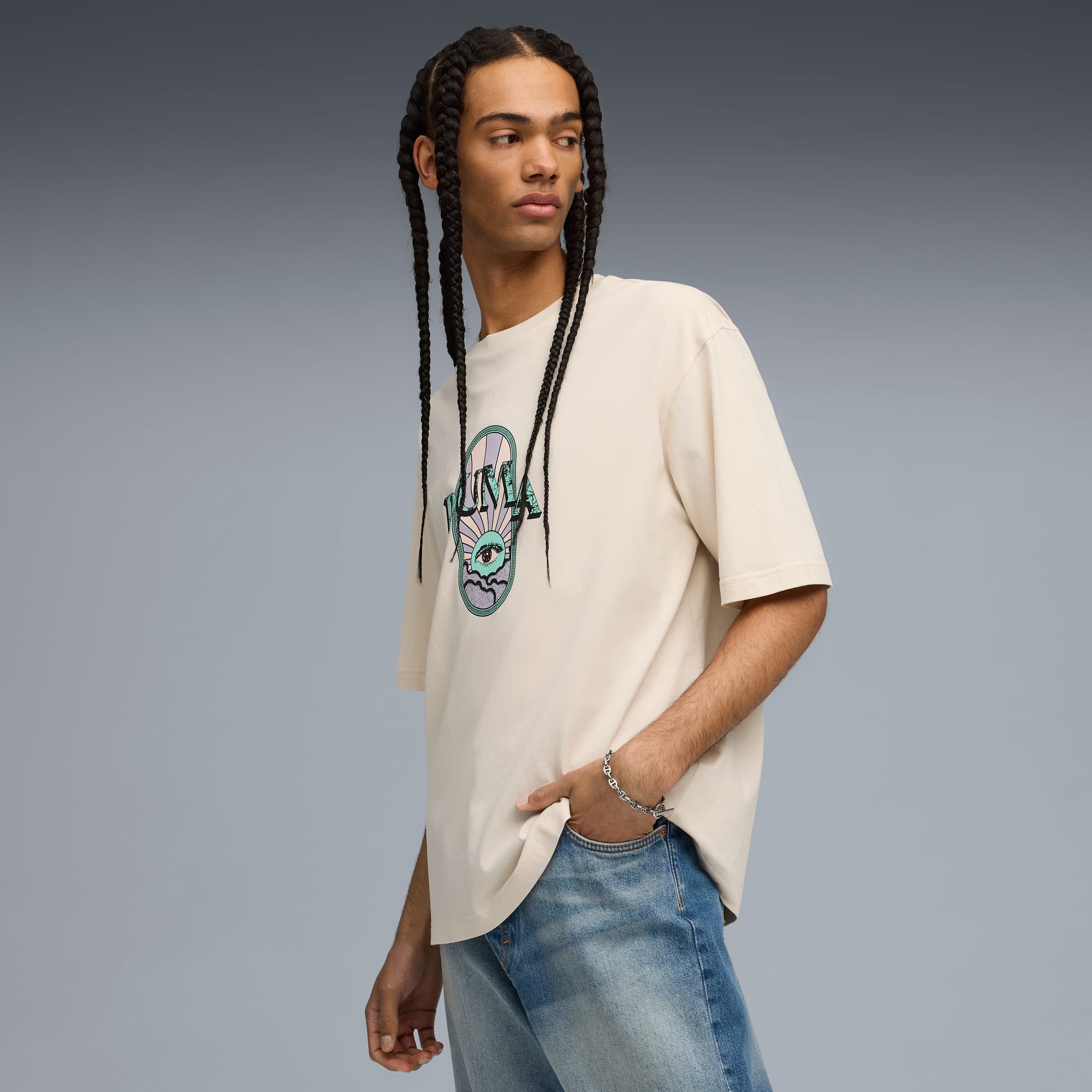 Tegen grijs, model poseert in een grafisch T-shirt en jeans, hand in zak.