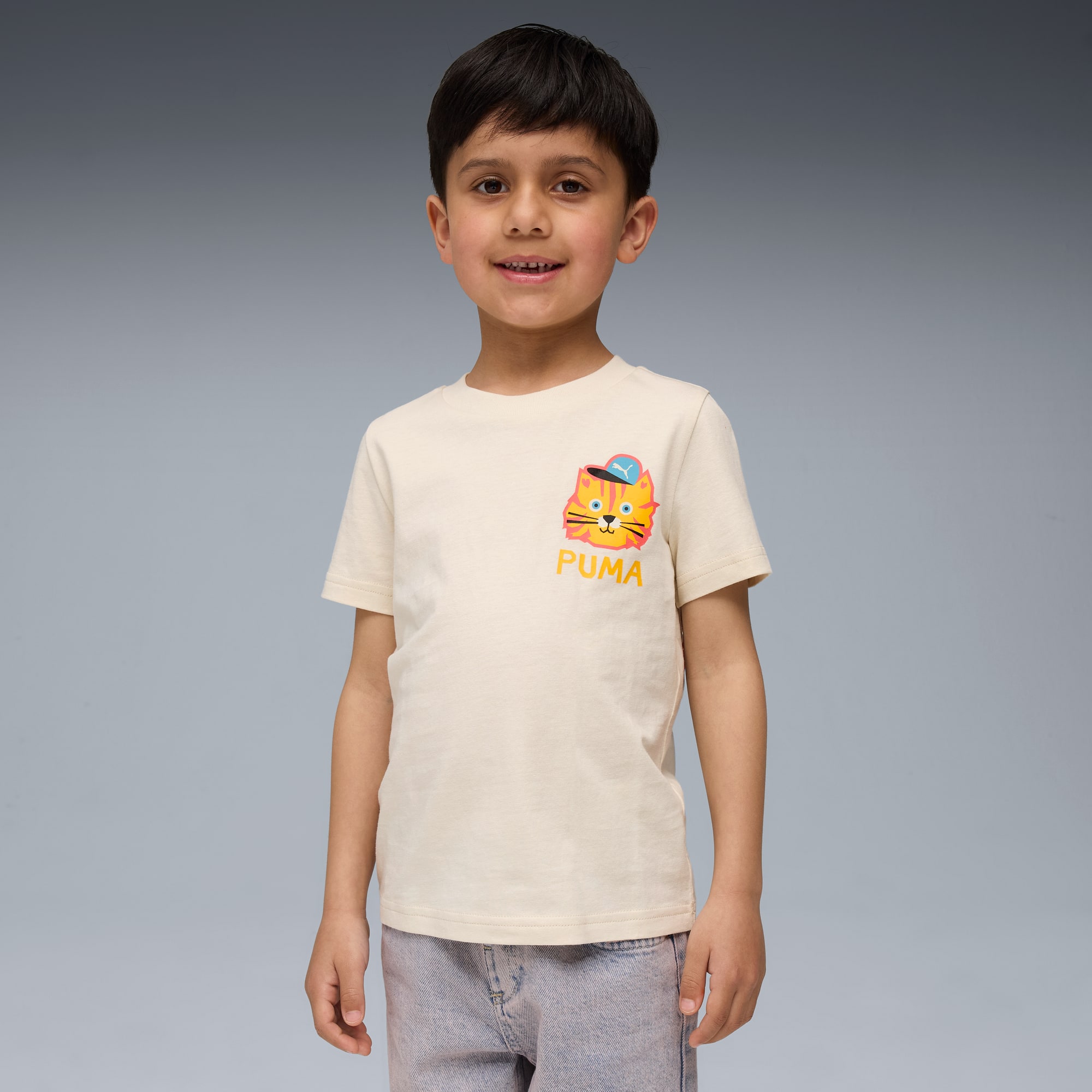 Ein Kind lächelt vor einem grauen Hintergrund und trägt ein helles T-Shirt mit Katzenaufdruck.