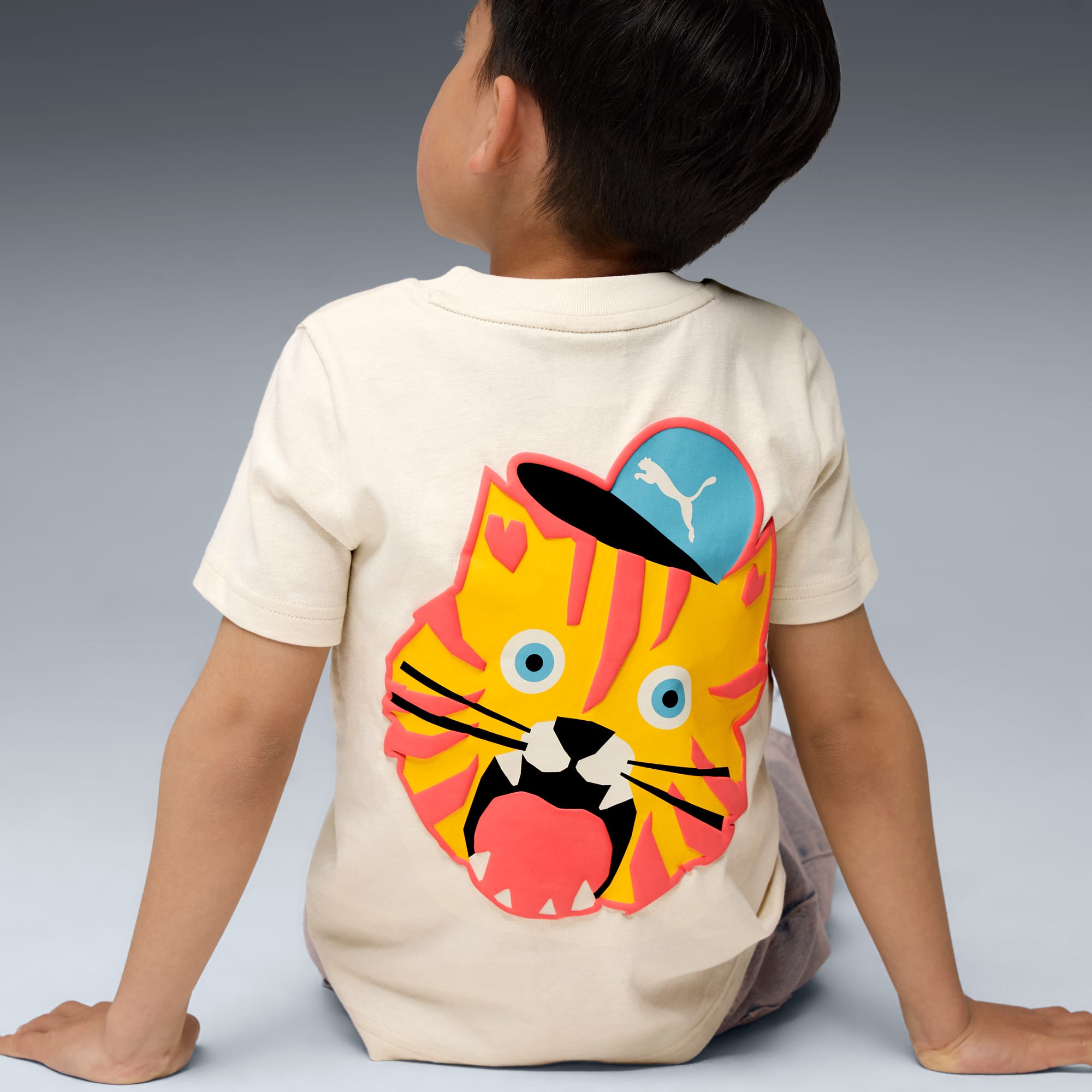 Ein Kind sitzt vor grauem Hintergrund und trägt ein T-Shirt mit Tigergrafik.