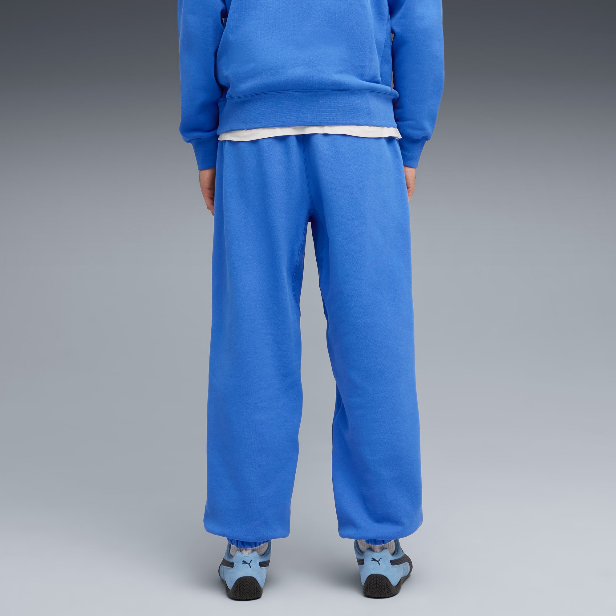 Un modèle, dos à l'objectif sur fond gris, porte un survêtement bleu avec t-shirt blanc et chaussures de course bleues.