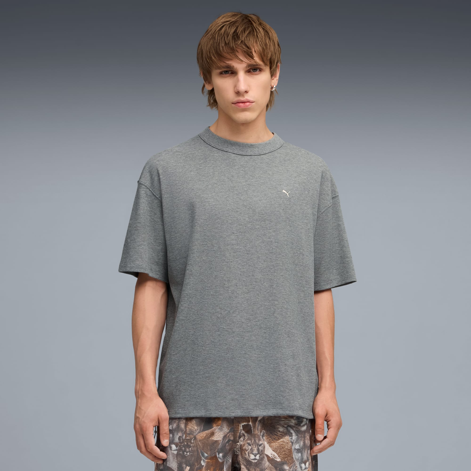 Un modèle pose sur un fond gris, portant un t-shirt gris et un short imprimé.