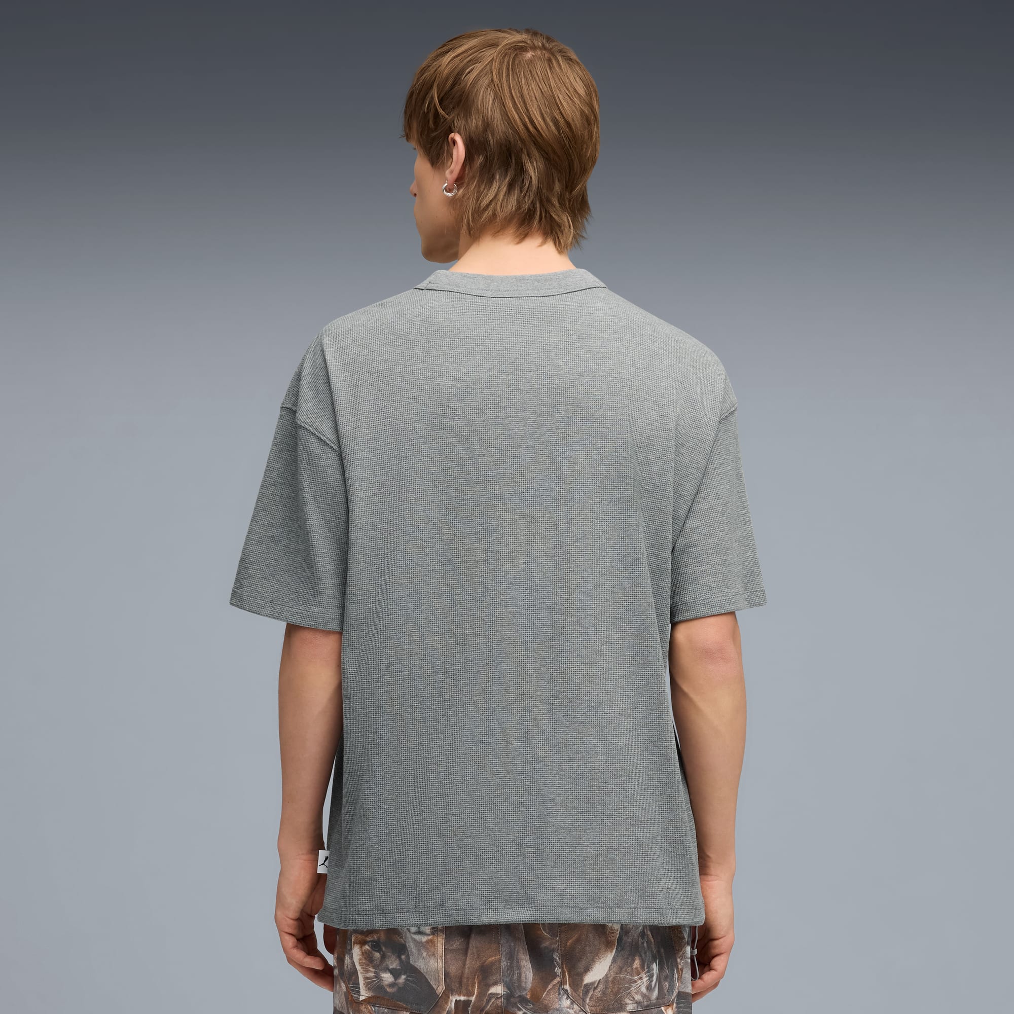 Un modèle, de dos sur fond gris, porte un t-shirt gris et un short à motifs.