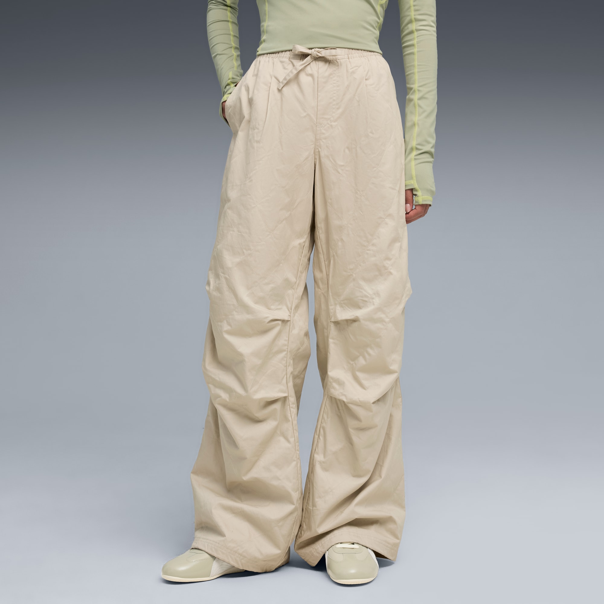 Un modèle pose sur fond gris, portant un pantalon beige, un haut vert clair et des chaussures assorties.