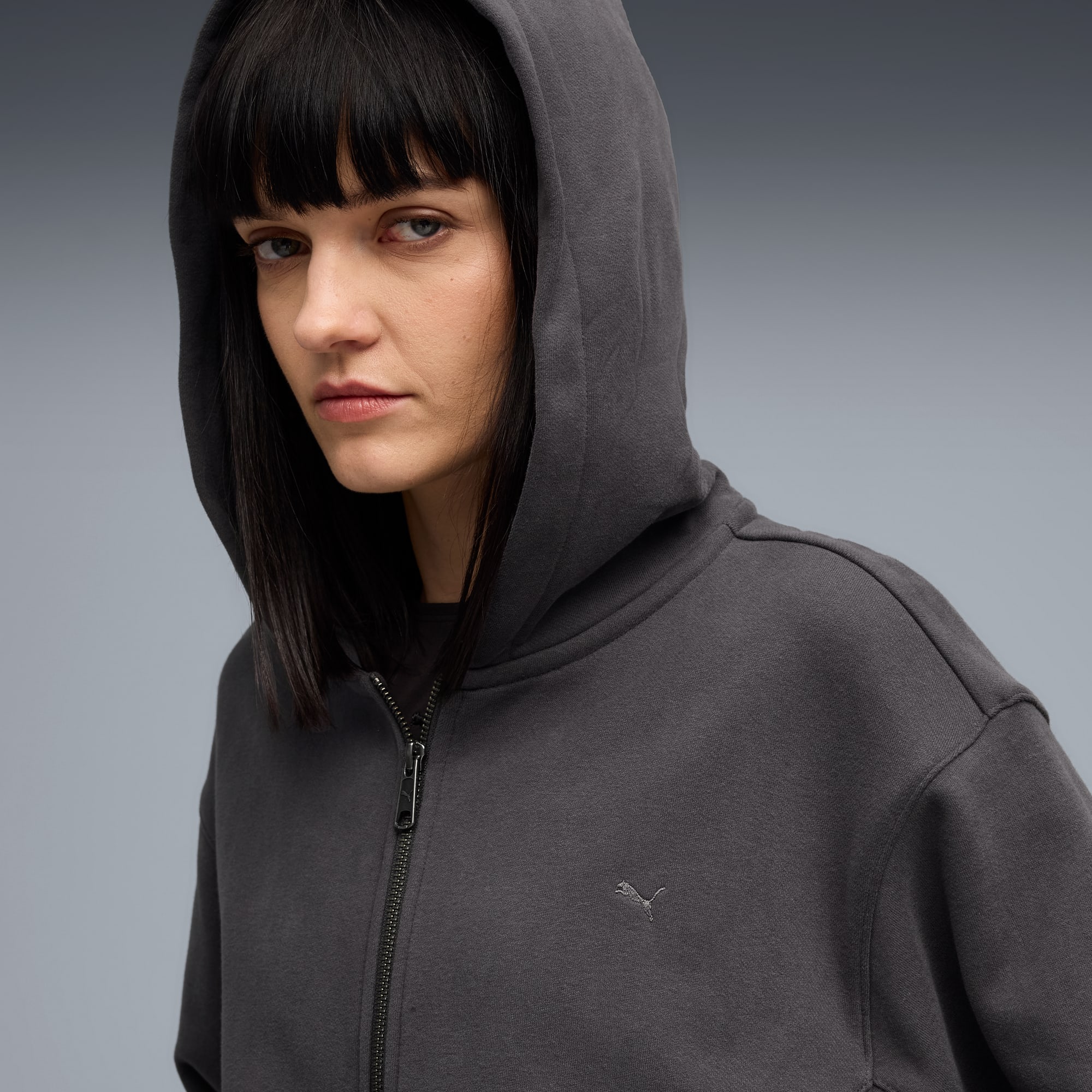Un mannequin en veste à capuche grise pose sur un fond gris.