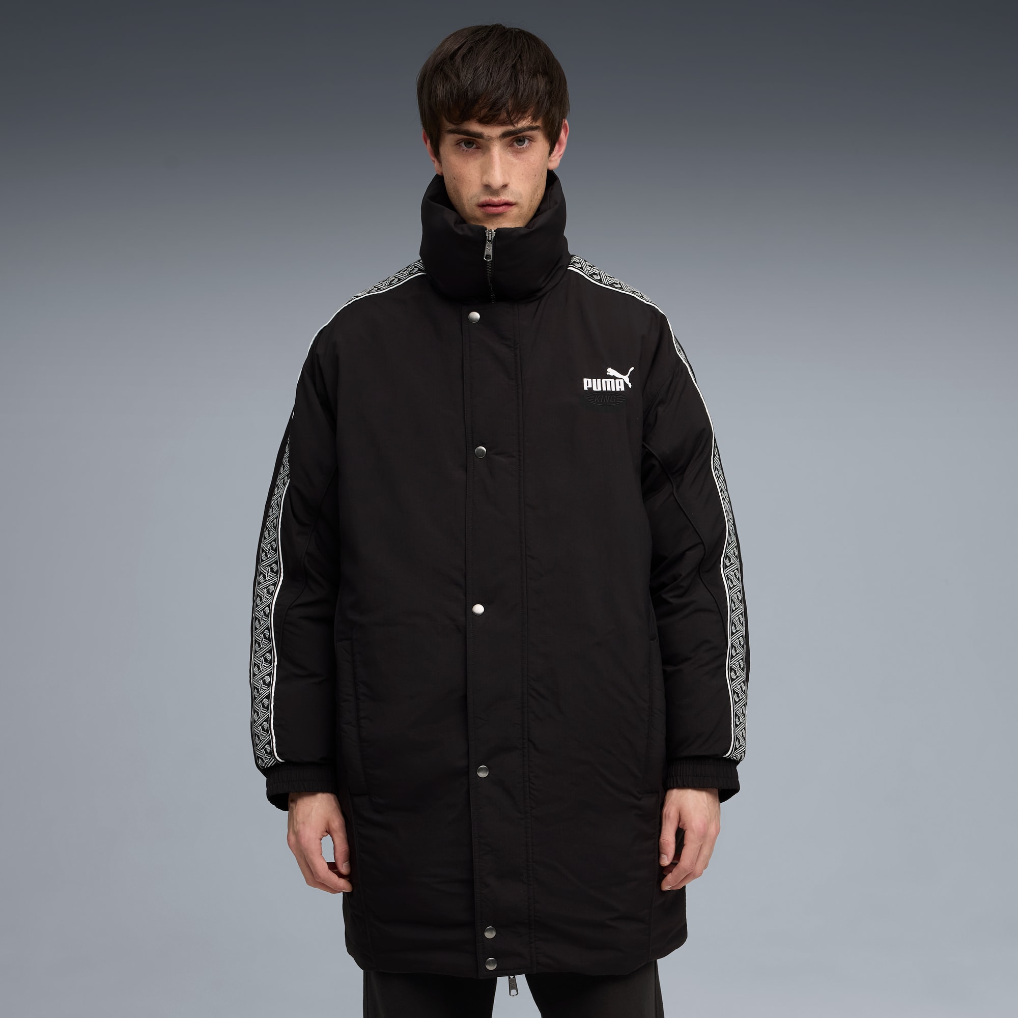 Tegen een grijze achtergrond poseert een model in een zwarte Puma jas met hoge kraag en mouwpatroon.