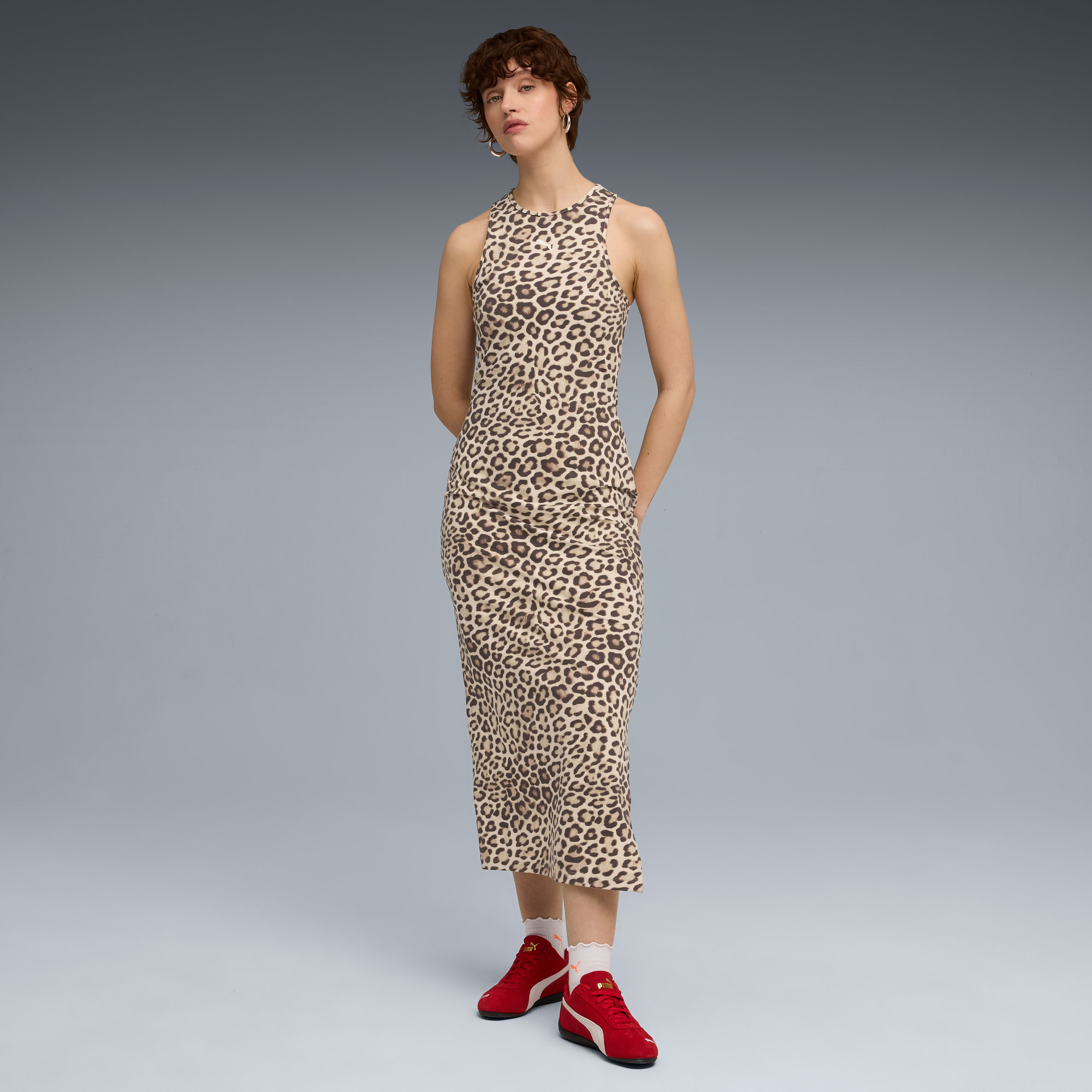 Su sfondo grigio, modella in abito leopardato e scarpe da ginnastica rosse.