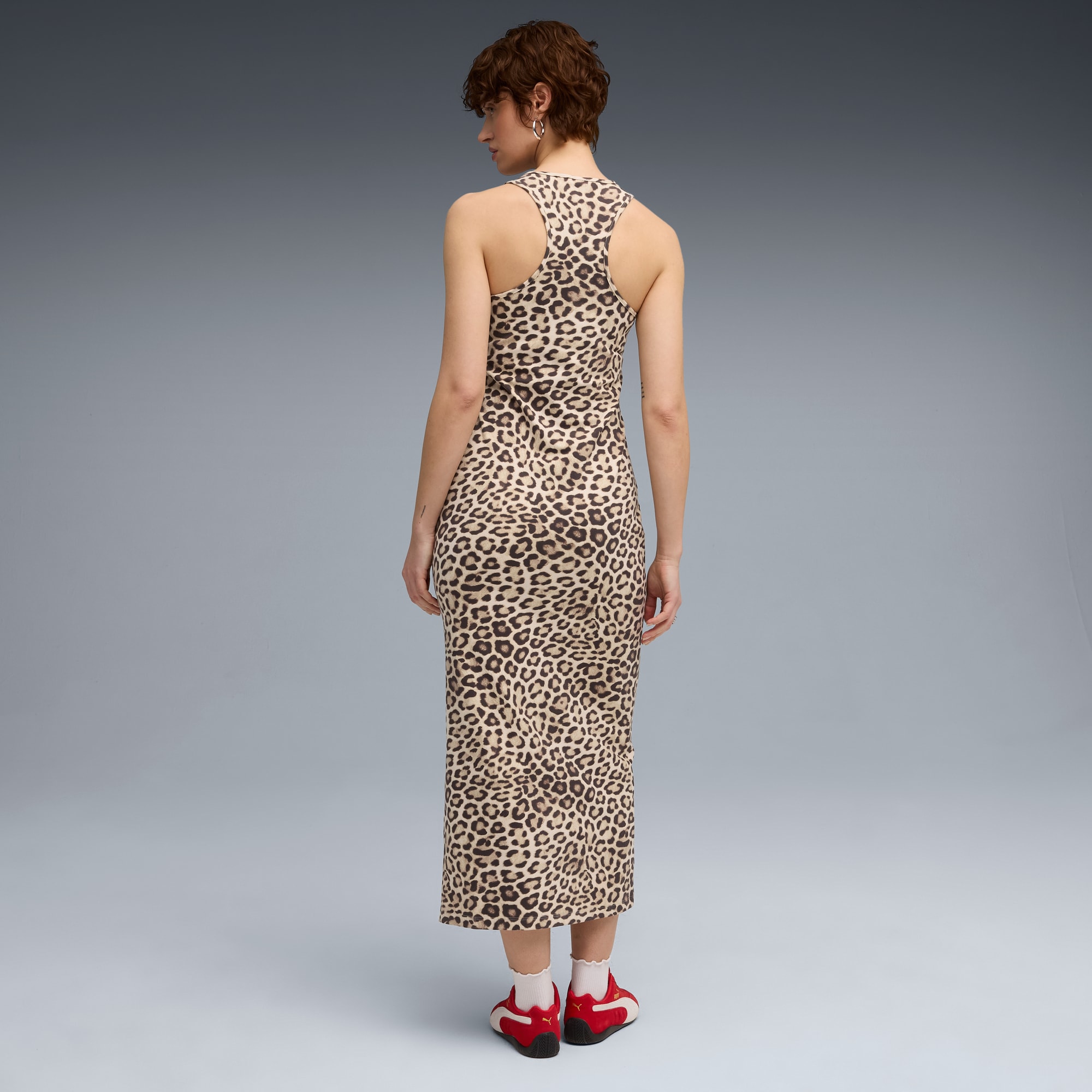Una modella di spalle su sfondo grigio indossa un abito leopardato e scarpe da ginnastica rosse.